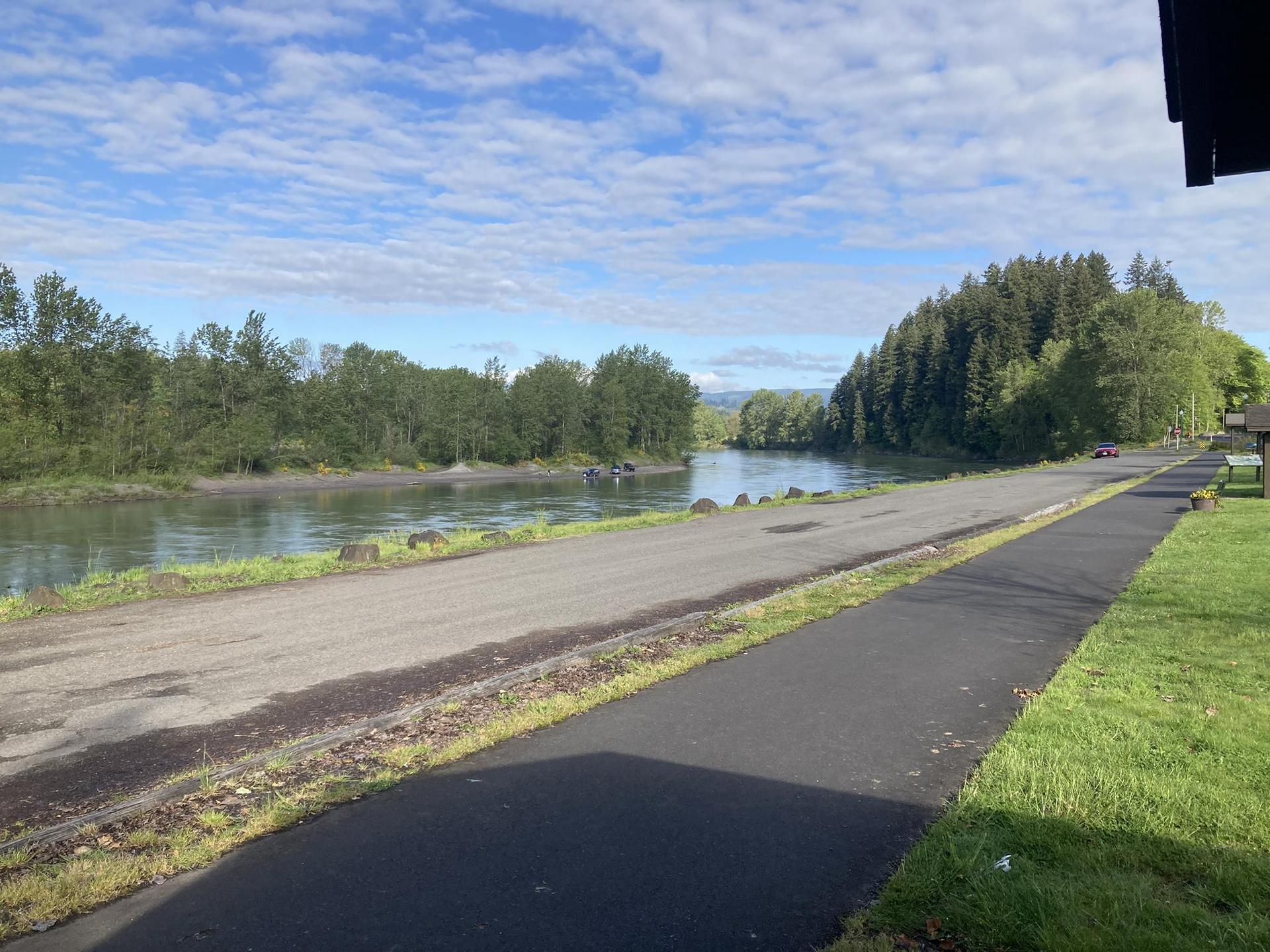 Paved path and dirt road alongside a wide river with forested banks.