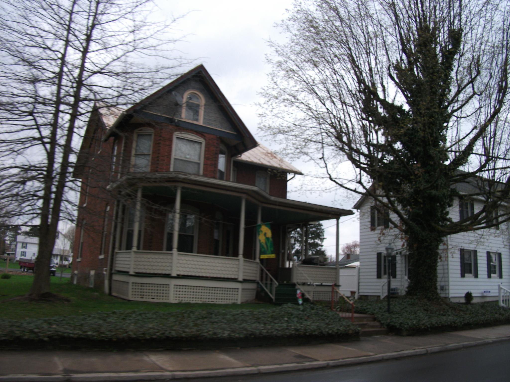 Two houses, one brick and one white, under an overcast sky with bare trees.