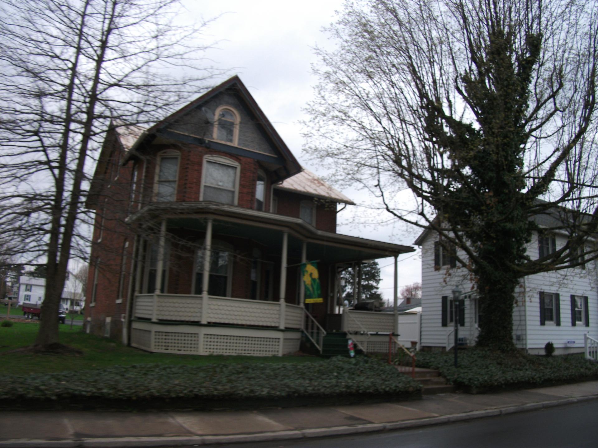 Two houses, one brick and one white, under an overcast sky with bare trees.