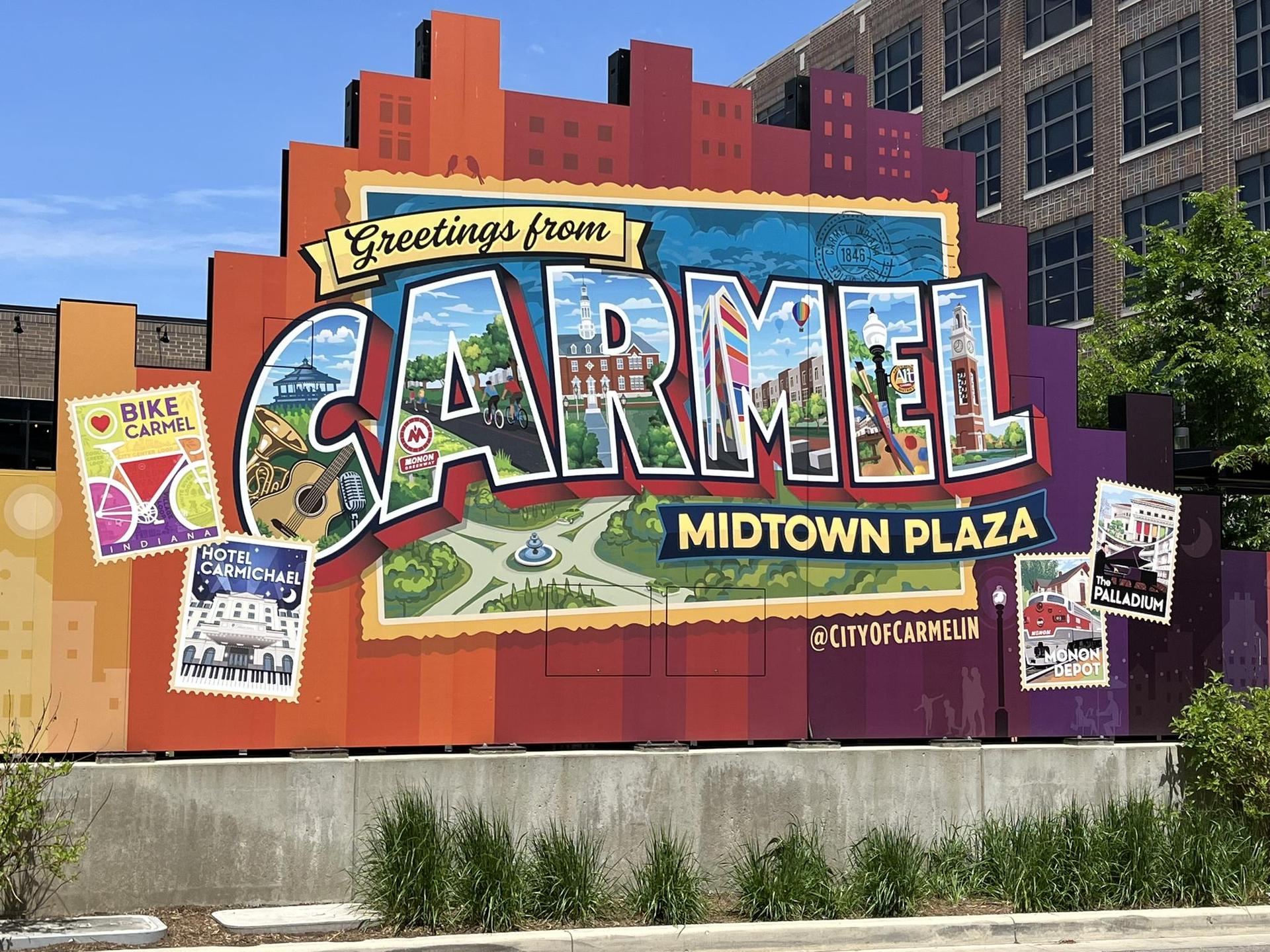 Large colorful postcard-style mural with "CARMEL" and local scenes on a sunny day.