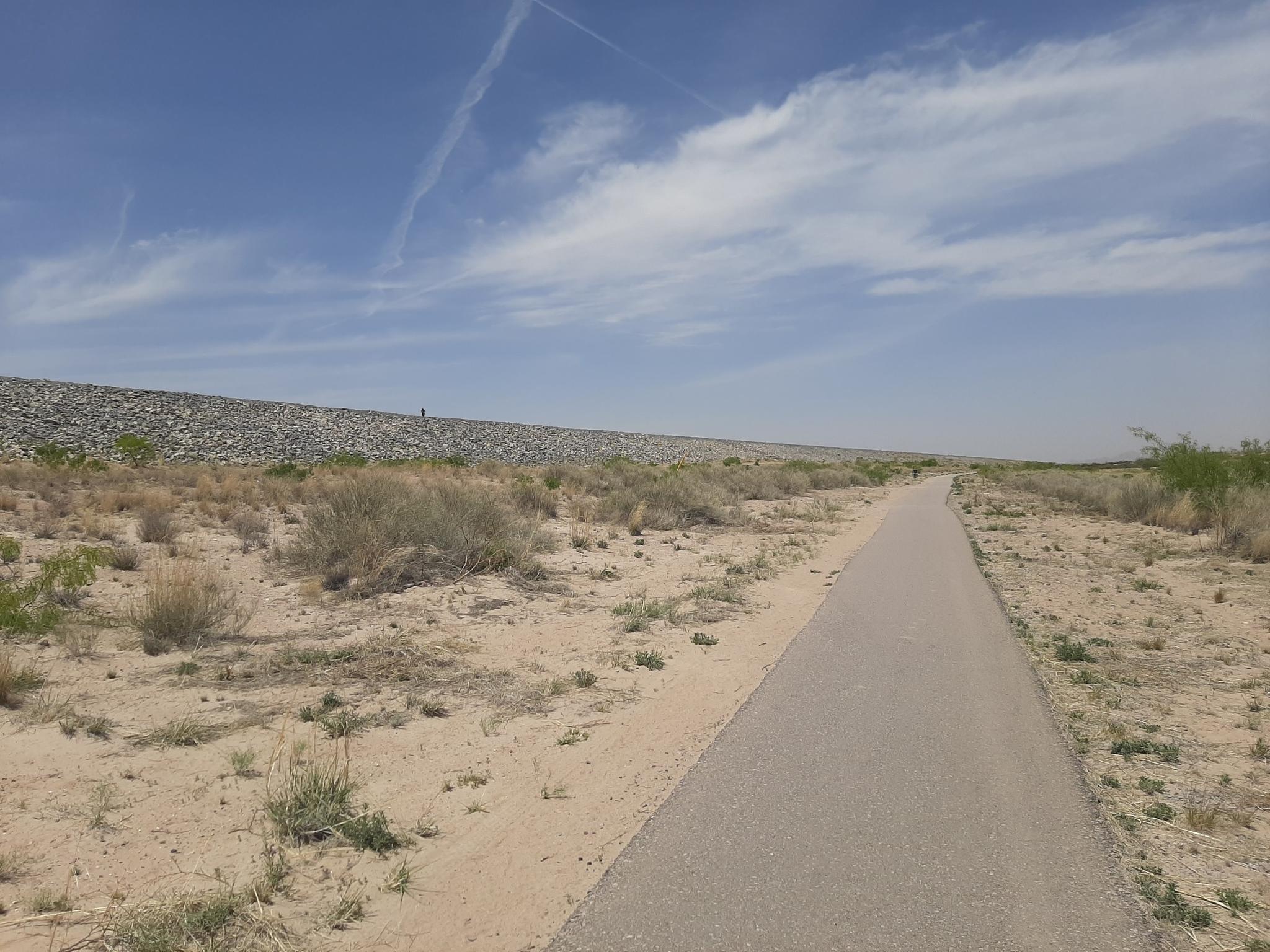 Paved path alongside a rocky embankment in a dry, sunny landscape.