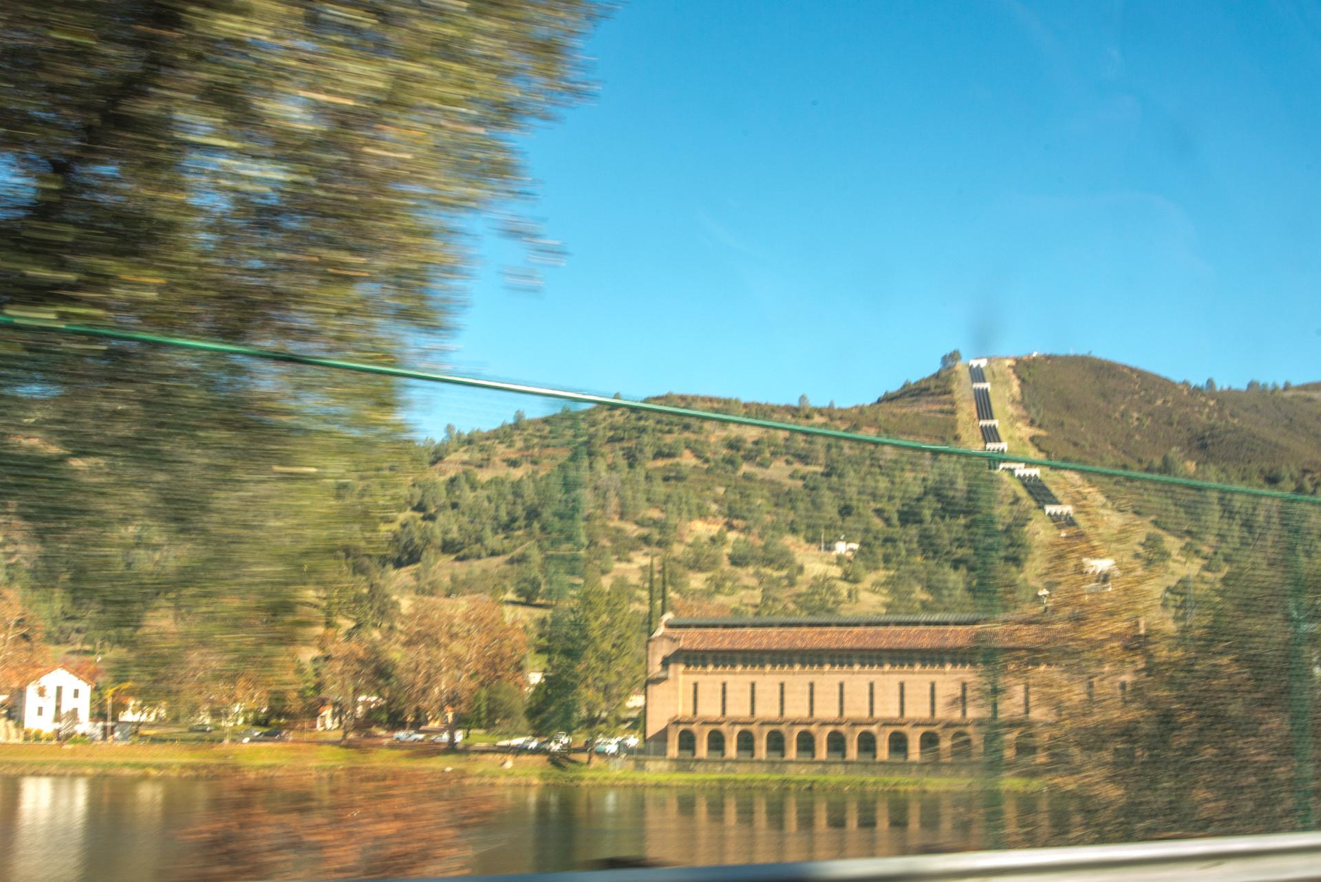 Motion-blurred trees frame a building by water, with a steep hill and structure.