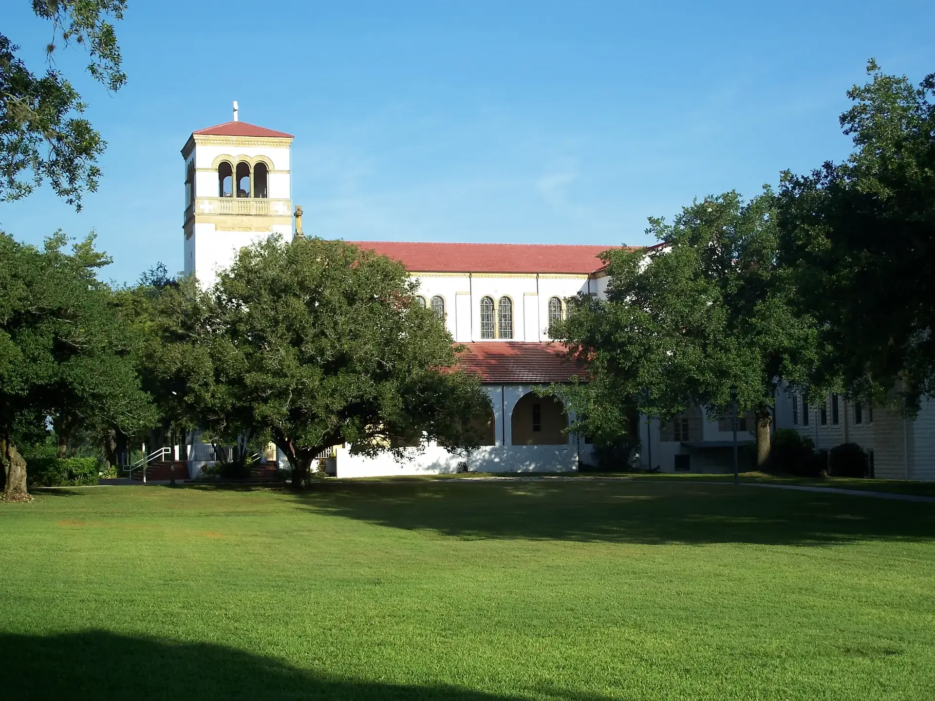 A large white building with a red roof and tower, surrounded by green trees.