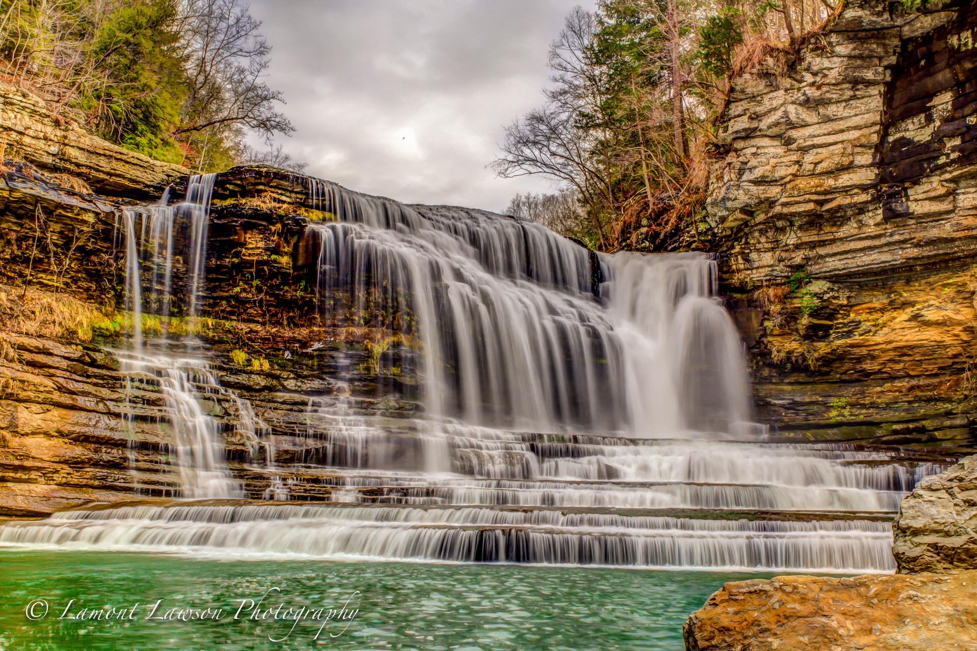 Majestic multi-tiered waterfall cascading over rocky cliffs into a green pool.
