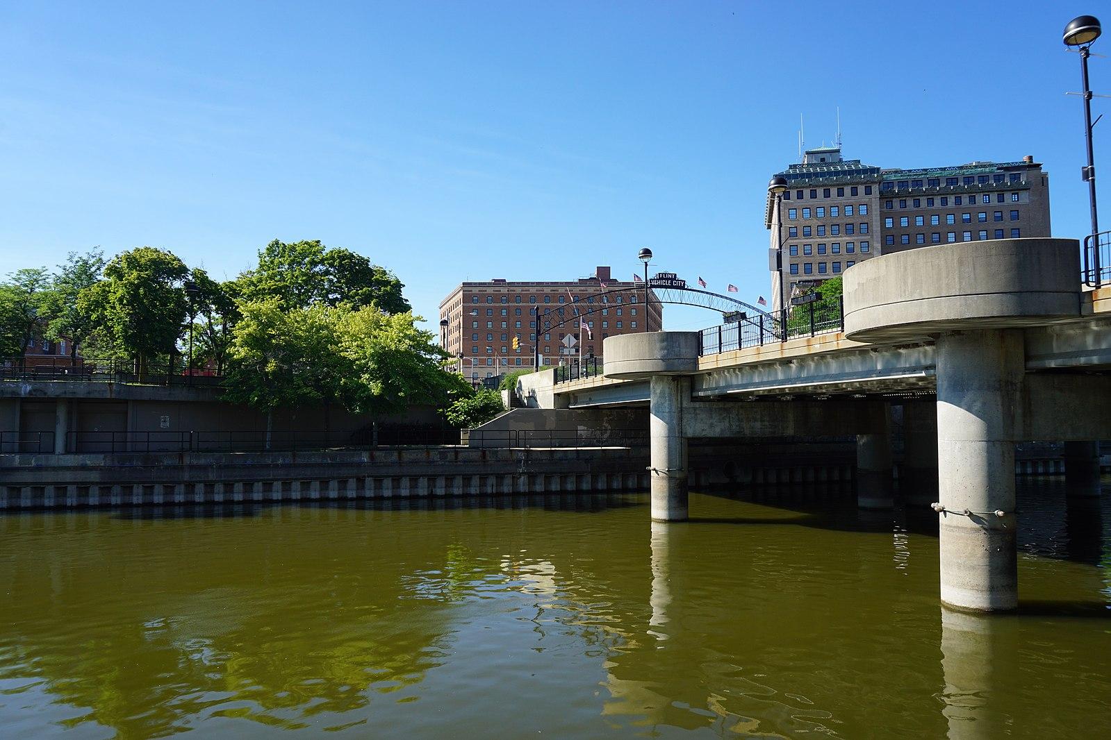 A river with a concrete bridge and distant buildings under a clear blue sky.