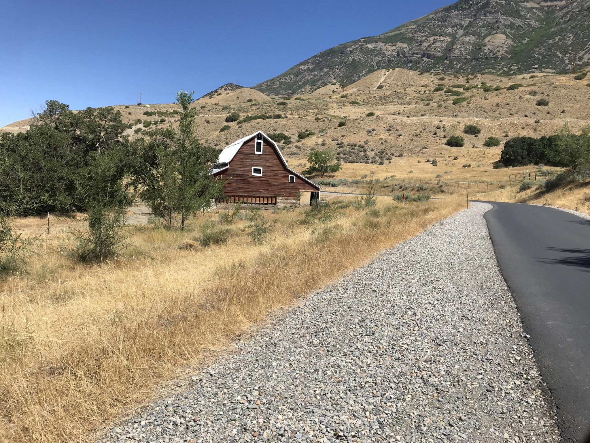 A rustic red barn sits in dry grass with mountains under clear sky.