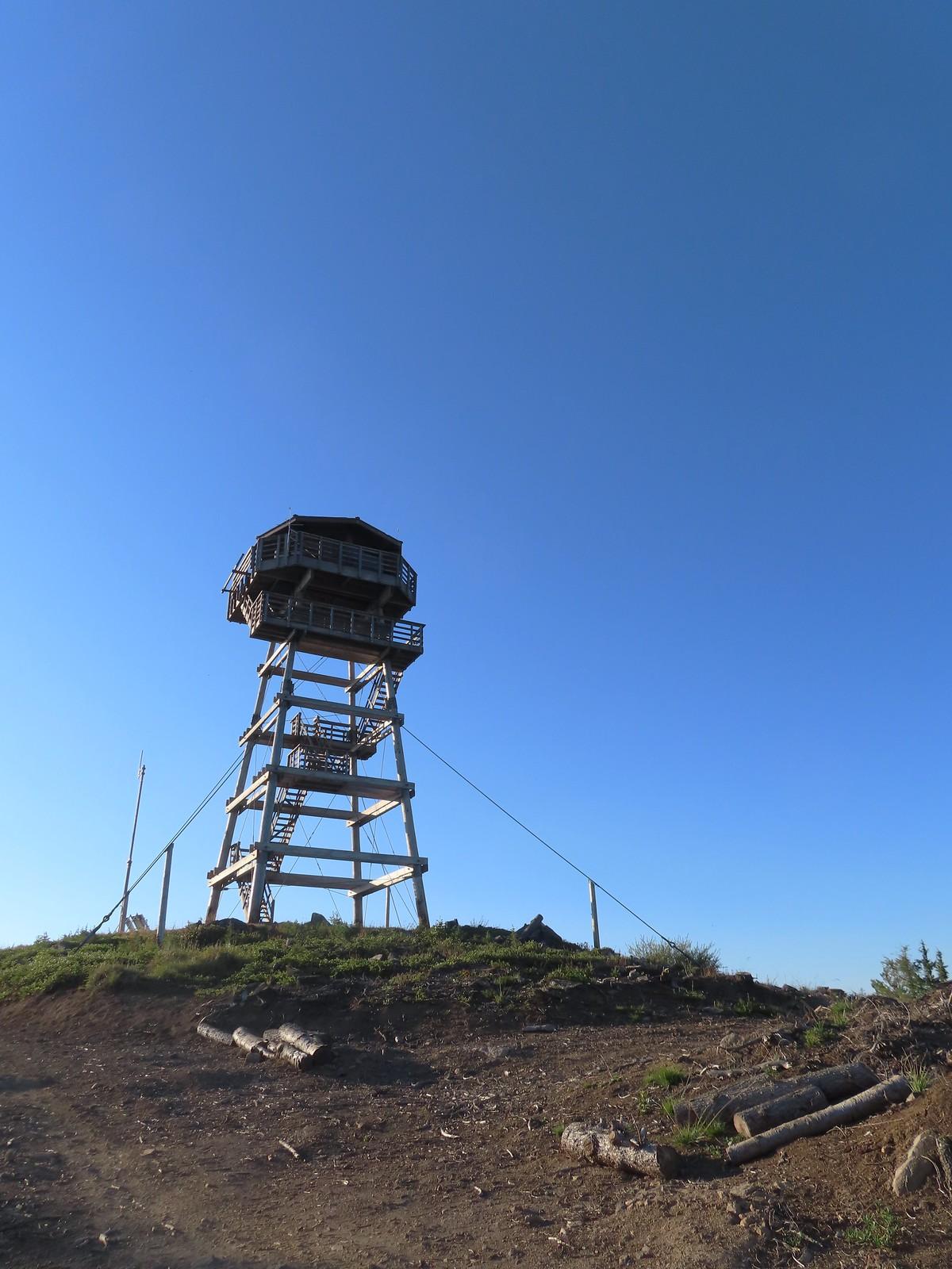 A tall wooden observation tower stands on a dirt hill under a clear blue sky.