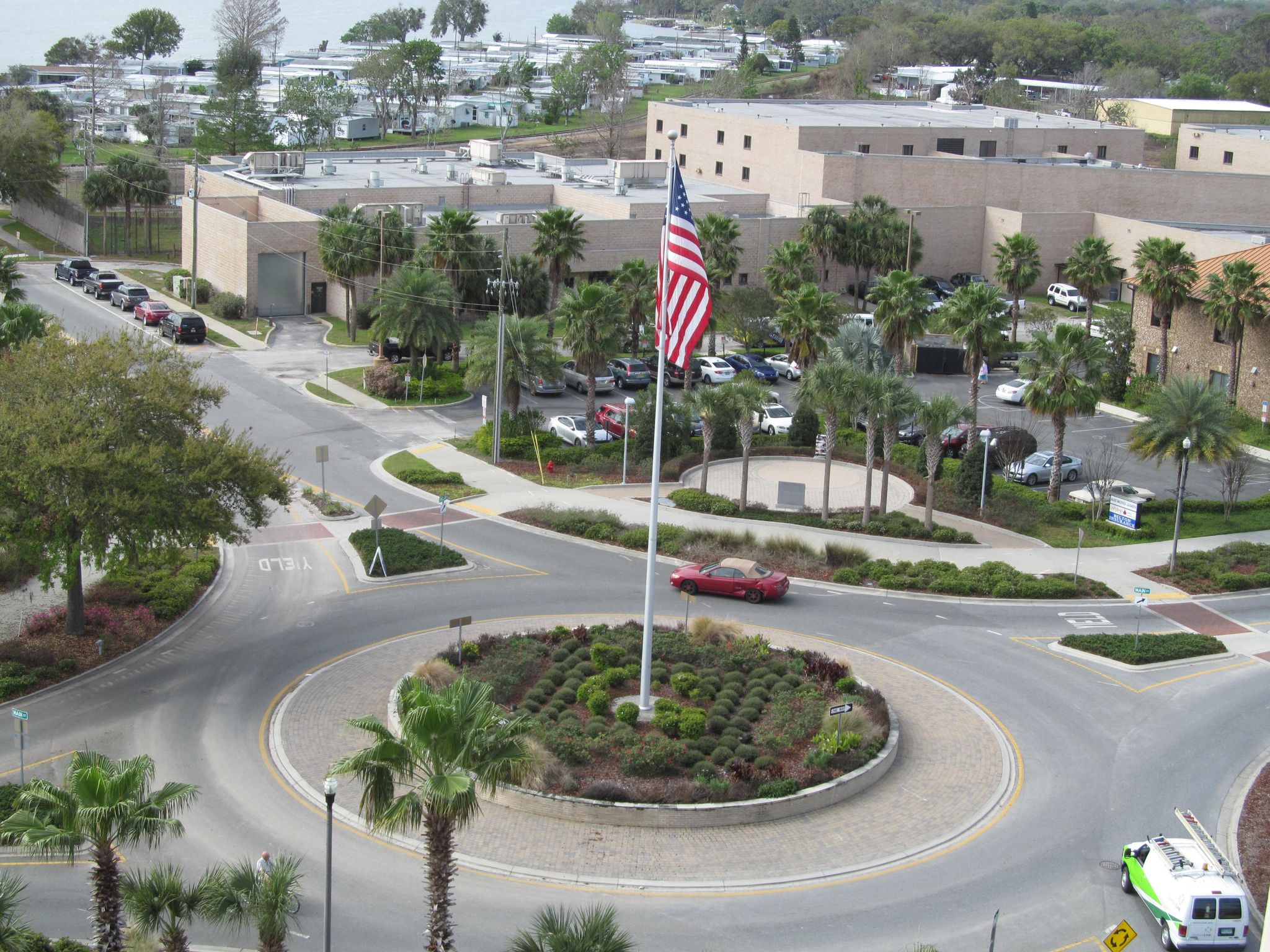 Aerial view of a roundabout with a large flag, surrounded by buildings and palm trees. - Tavares roundabout – Grantham Pointe Park loop from Tavares