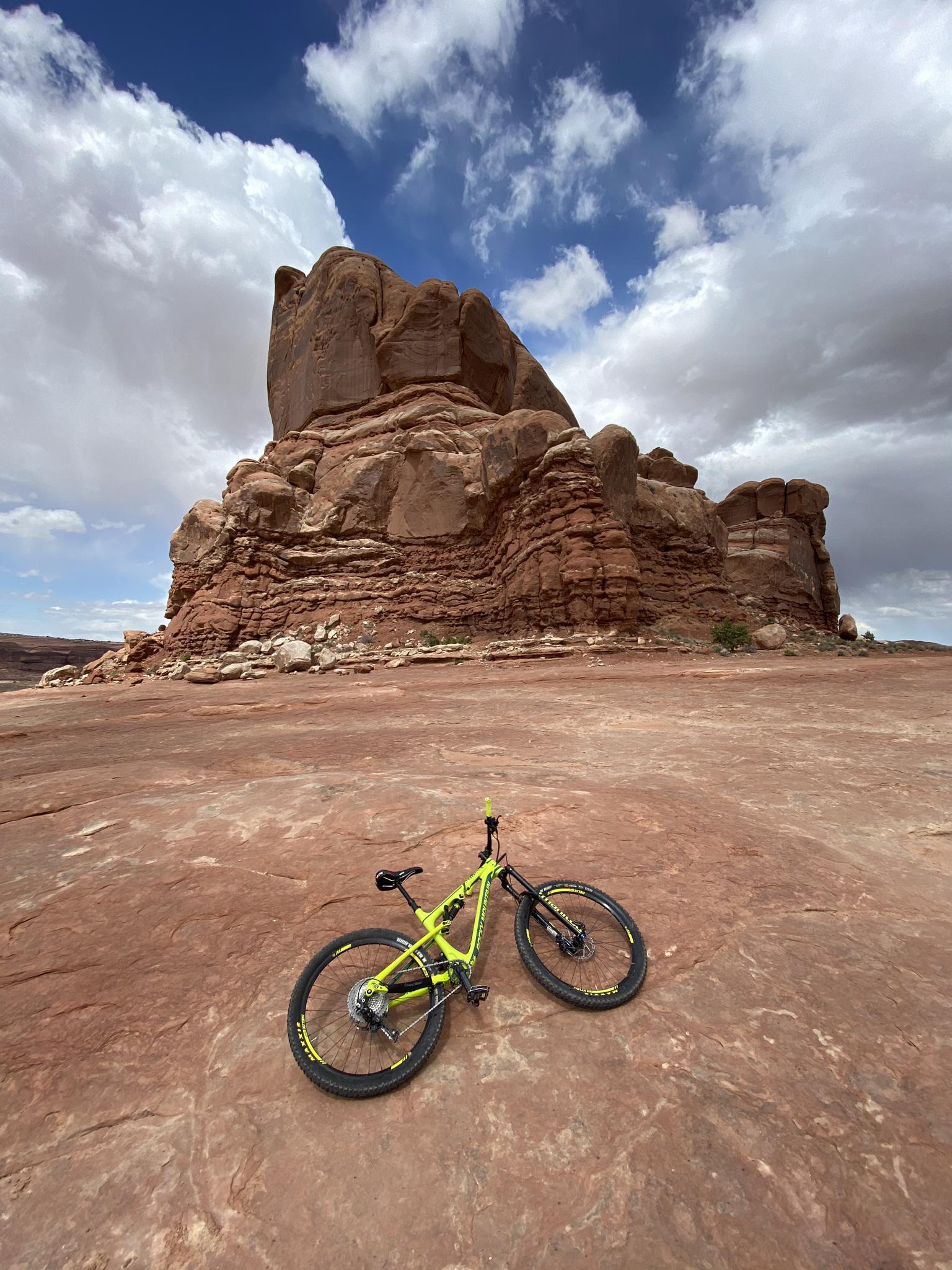 A yellow mountain bike rests on red rock near a massive rock formation.