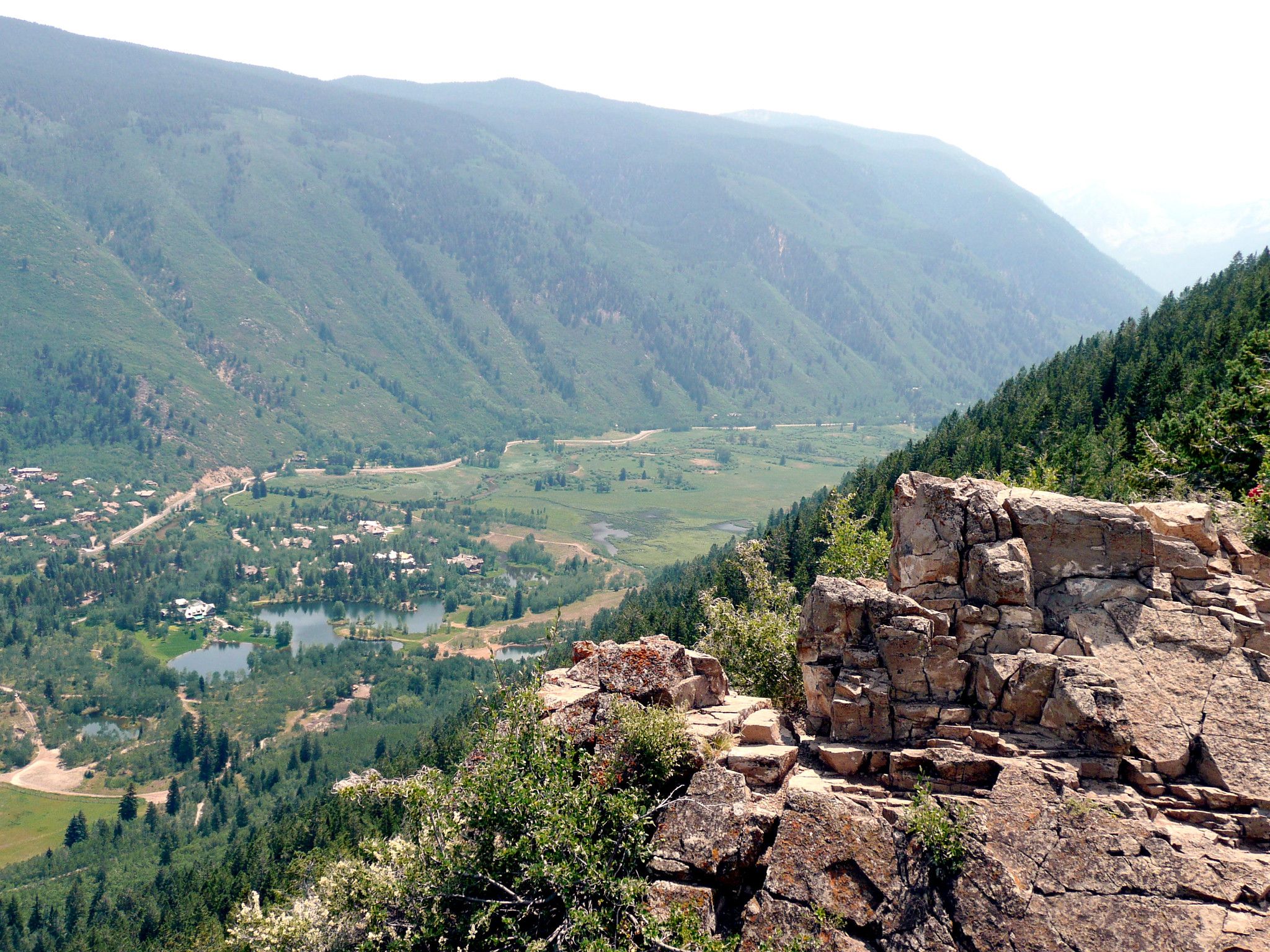 Rocky outcrop overlooks a green valley with a town and lakes. - Ute Trail