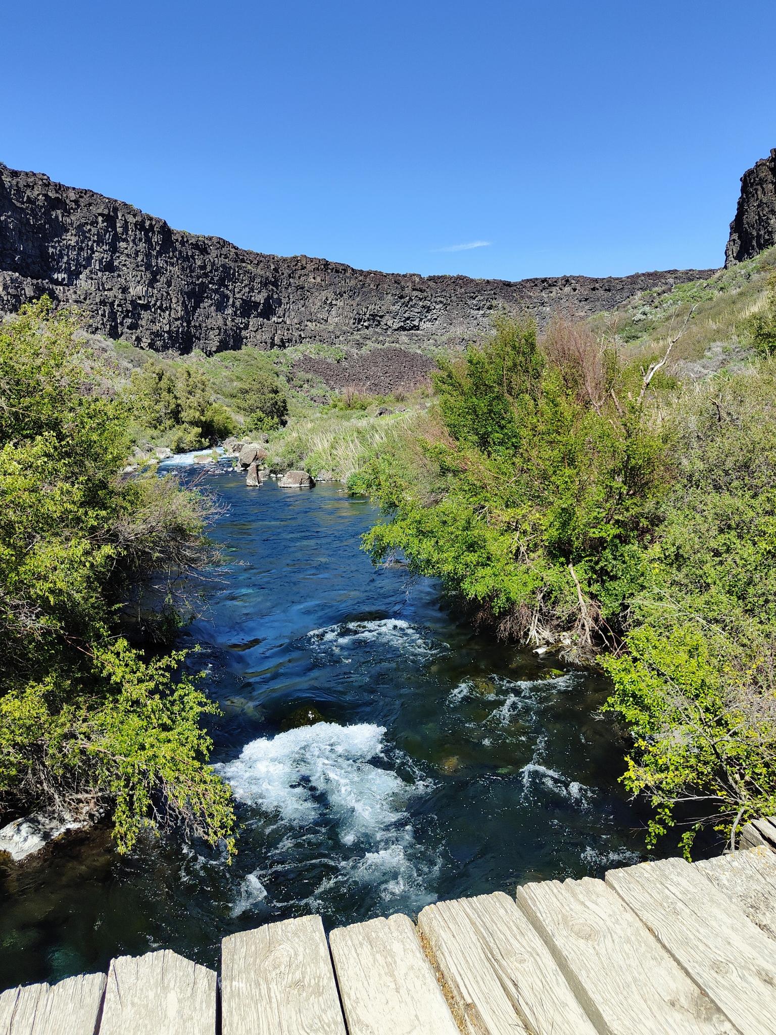 Rushing river seen from a wooden bridge, surrounded by rocky canyon walls.