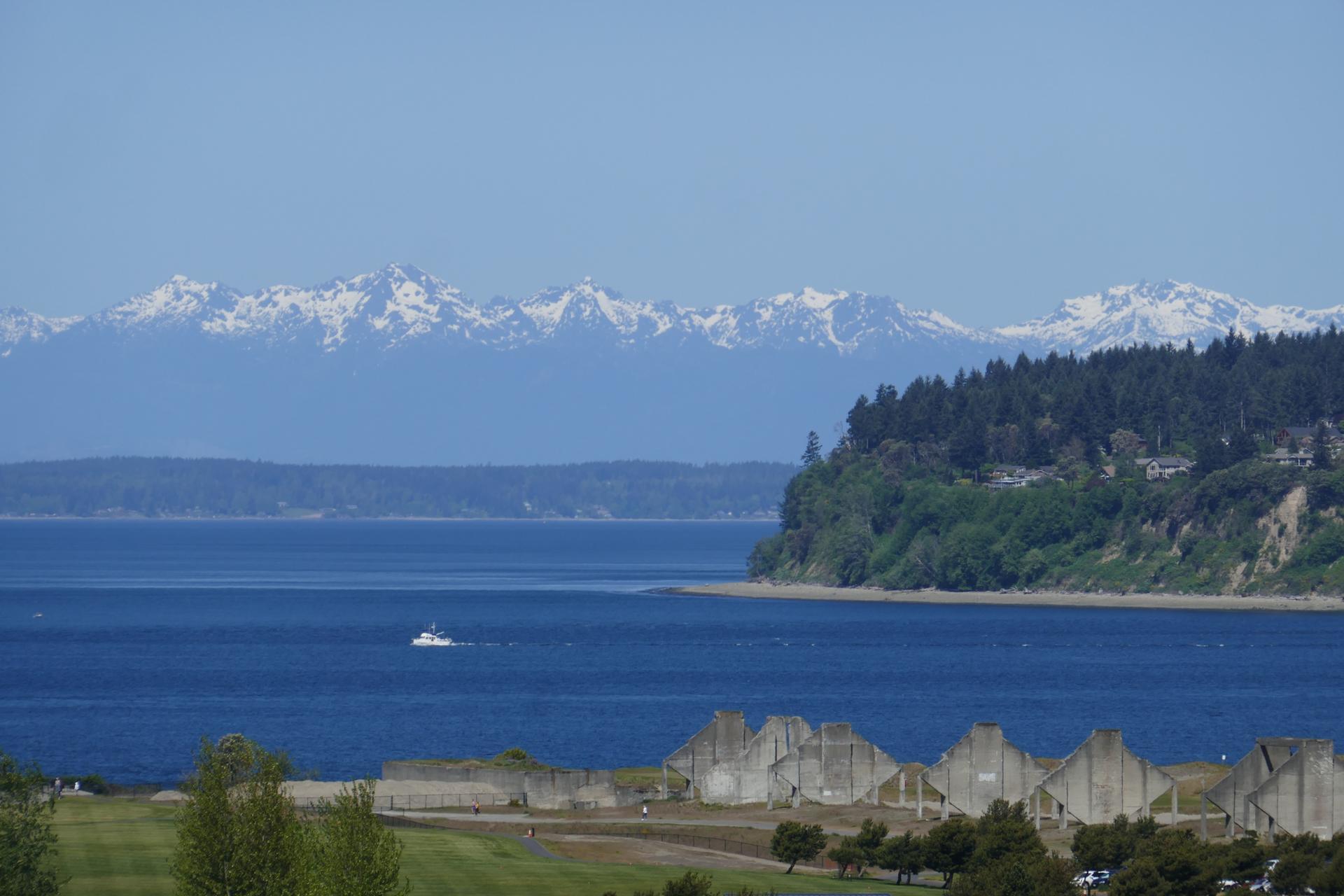 Sunny view of blue water, snow-capped mountains, and a boat, with ruins below.
