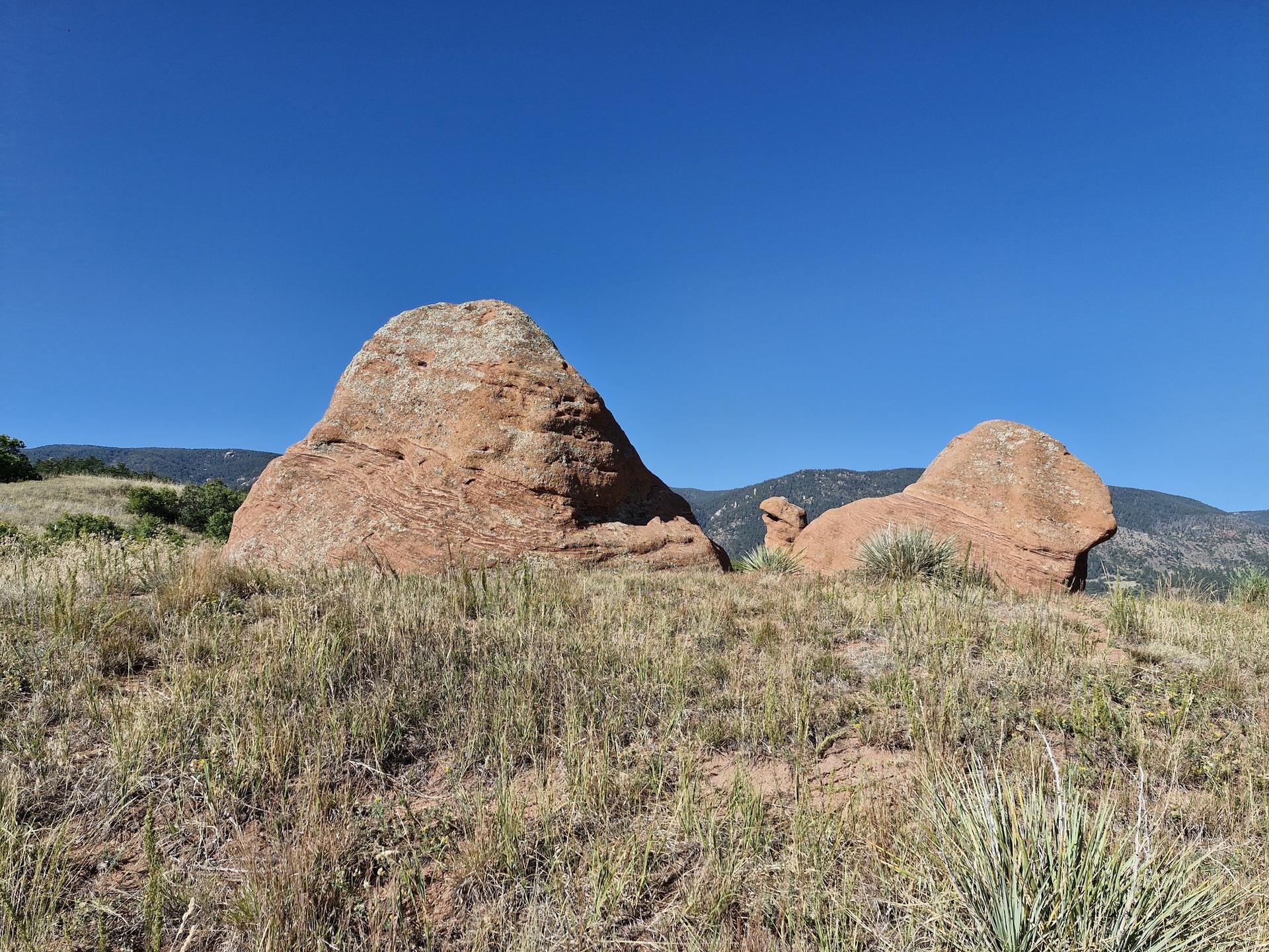 Two large red rock formations stand in a sunny, grassy field.