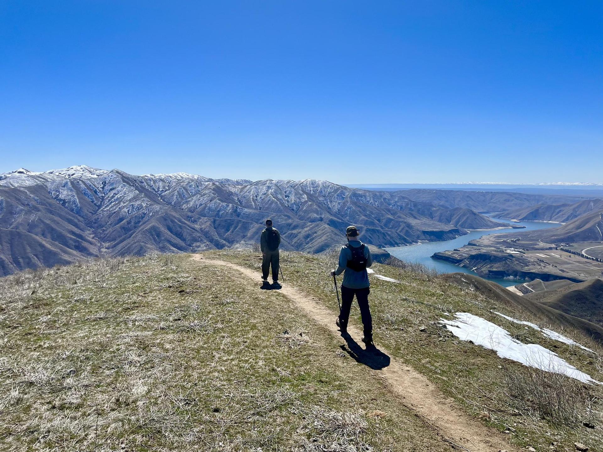Two hikers on a mountain ridge overlooking a river valley.