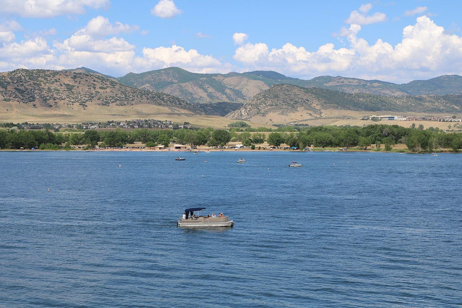 A pontoon boat on a large lake with distant mountains under a partly cloudy sky.
