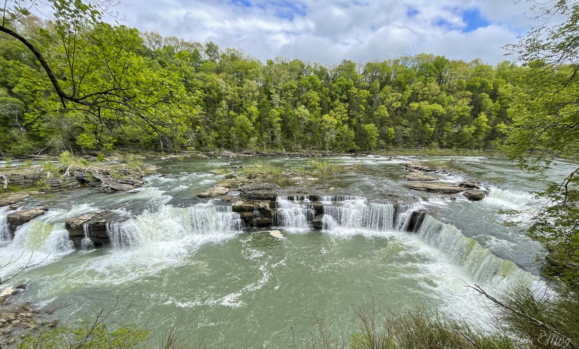 Wide, rocky waterfall cascades through a lush green forest.