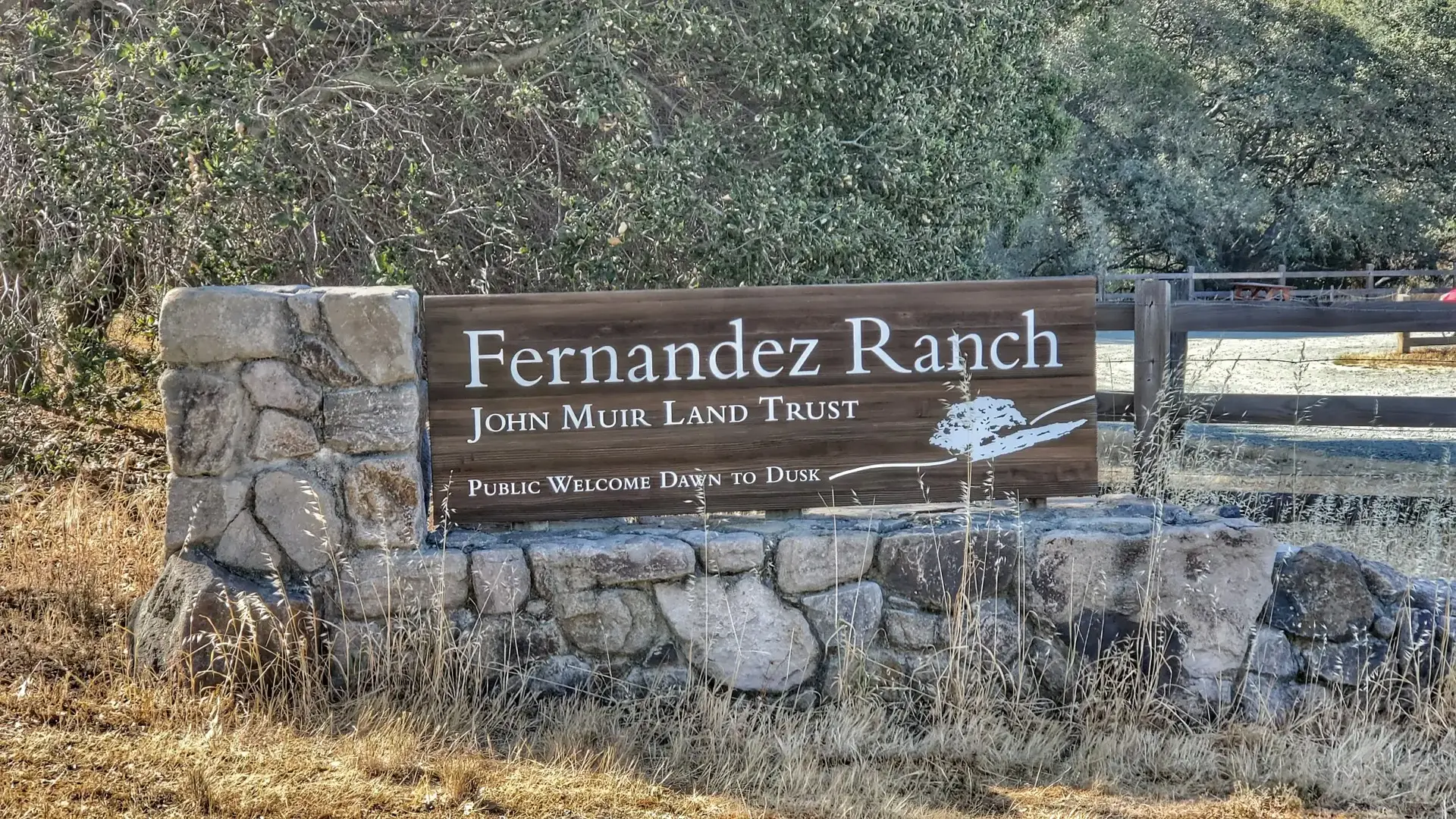 A rustic wooden sign on a stone base, surrounded by dry brush.
