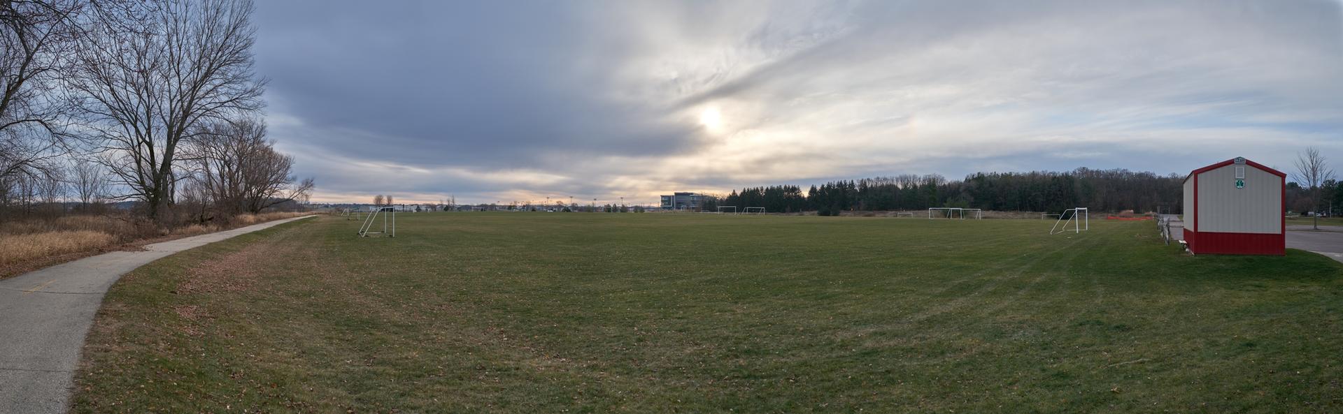 Panoramic view of a large grassy field with a path and building.