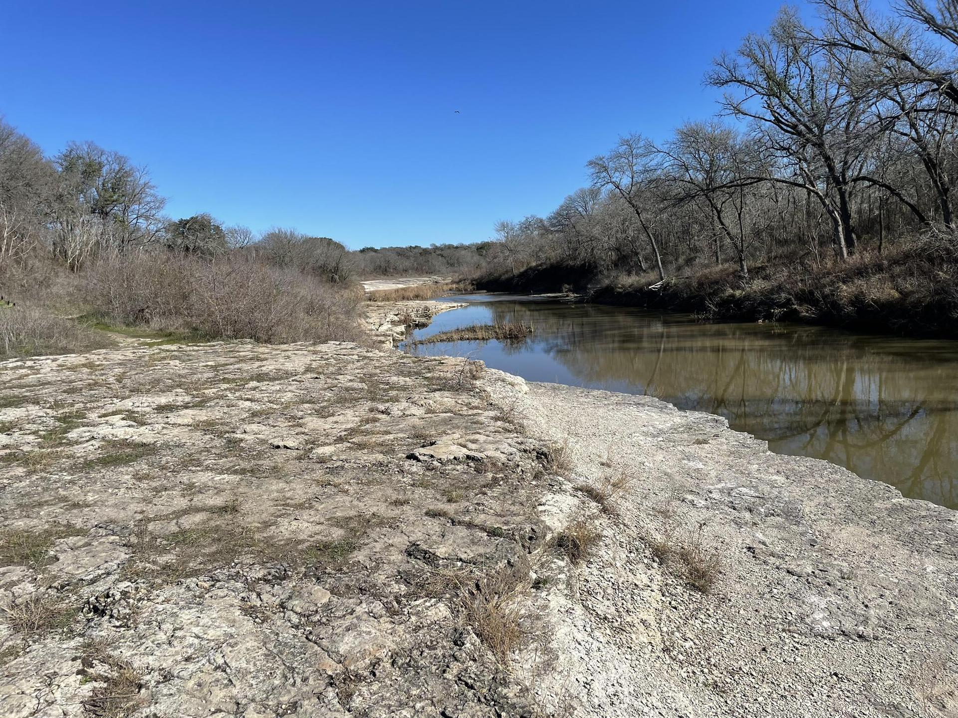 Wide river with rocky banks and bare trees under a clear blue sky.