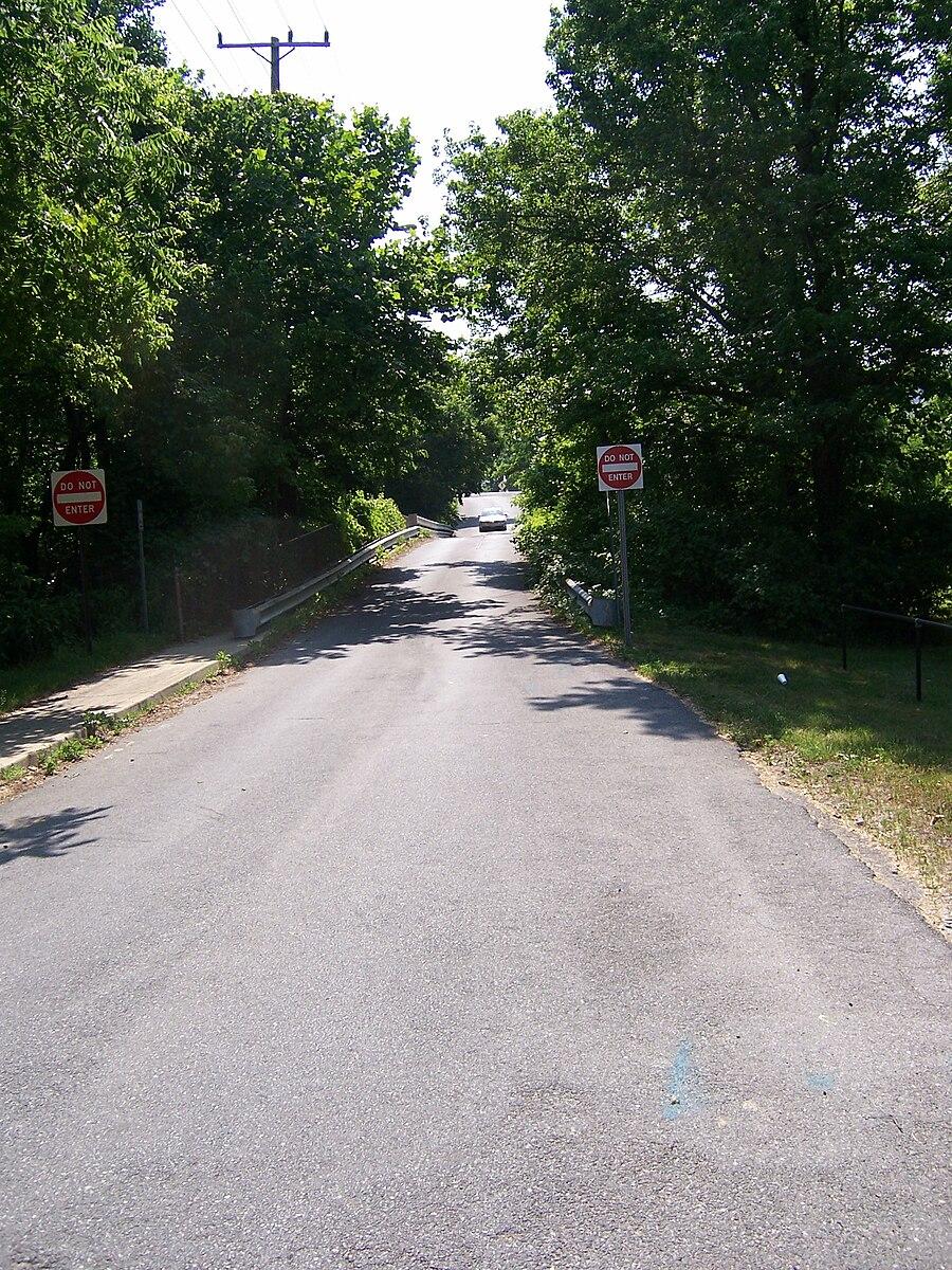An asphalt road goes uphill between trees with "Do Not Enter" signs.