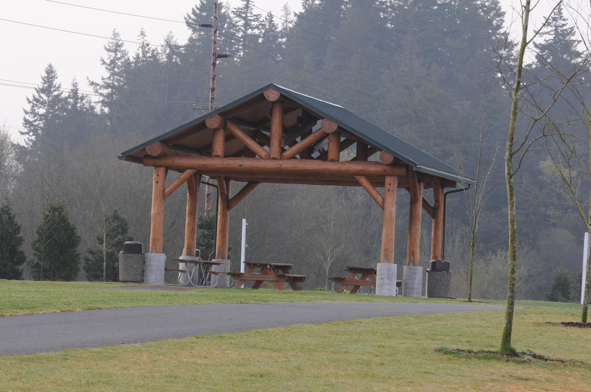 A large wooden picnic shelter with tables on a grassy field, overcast day.