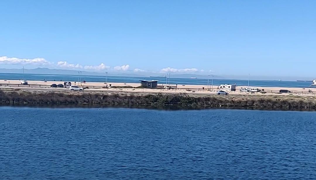 Wide blue water with a distant road and vehicles under clear sky.