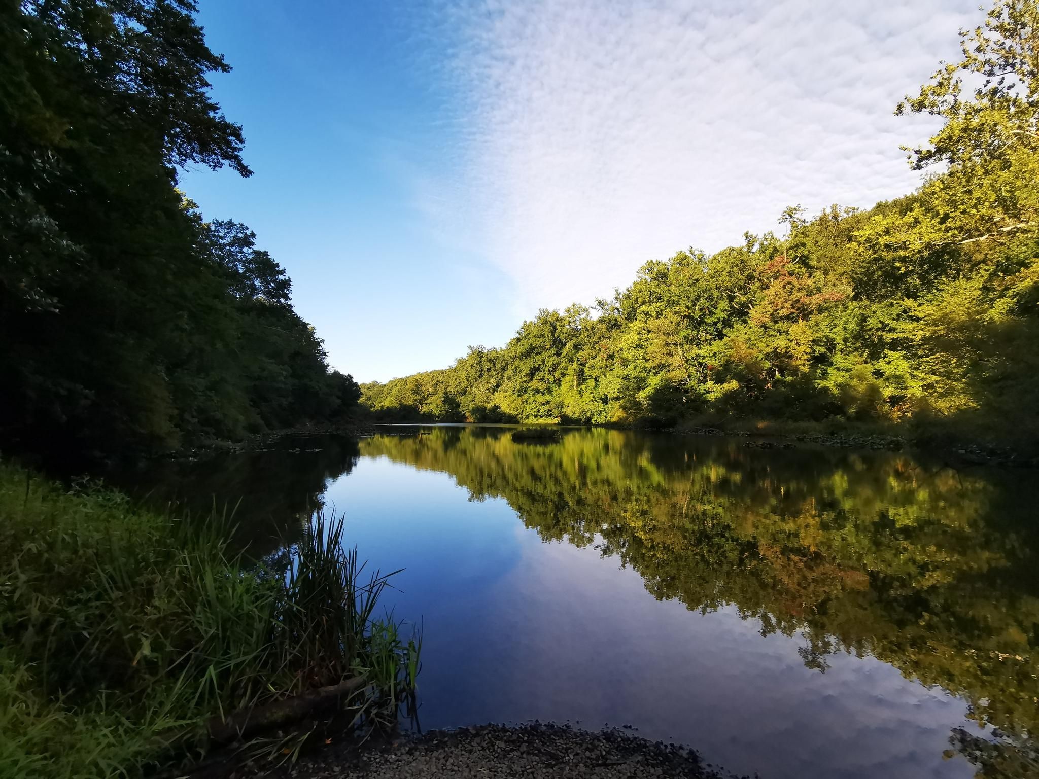 A serene lake reflects green hills and a blue sky with clouds. - Mindowaskin Park – Blue Brook Bridge loop from Roselle Park