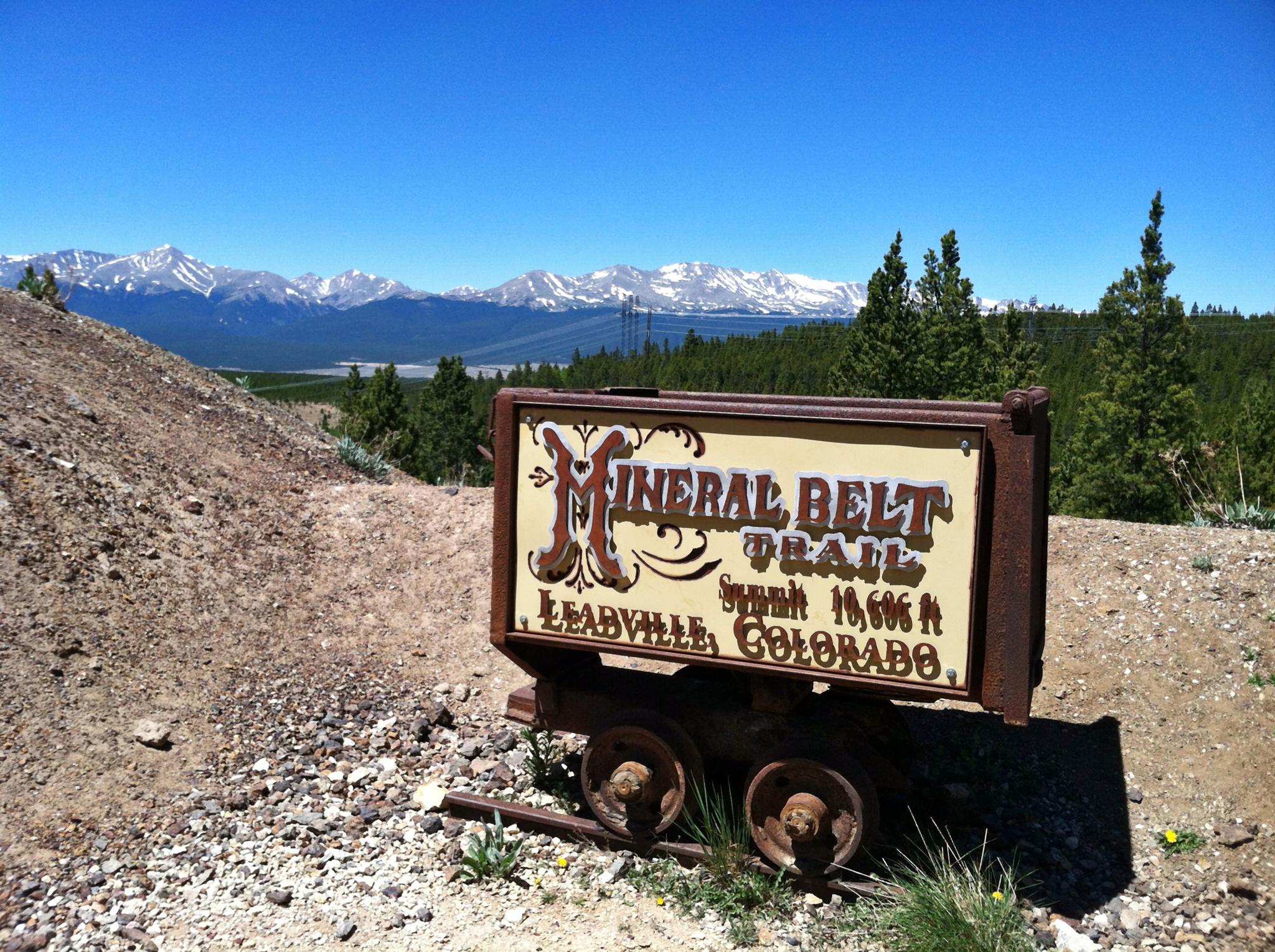 An old mining cart sign overlooks a vast landscape with distant snowy mountains.