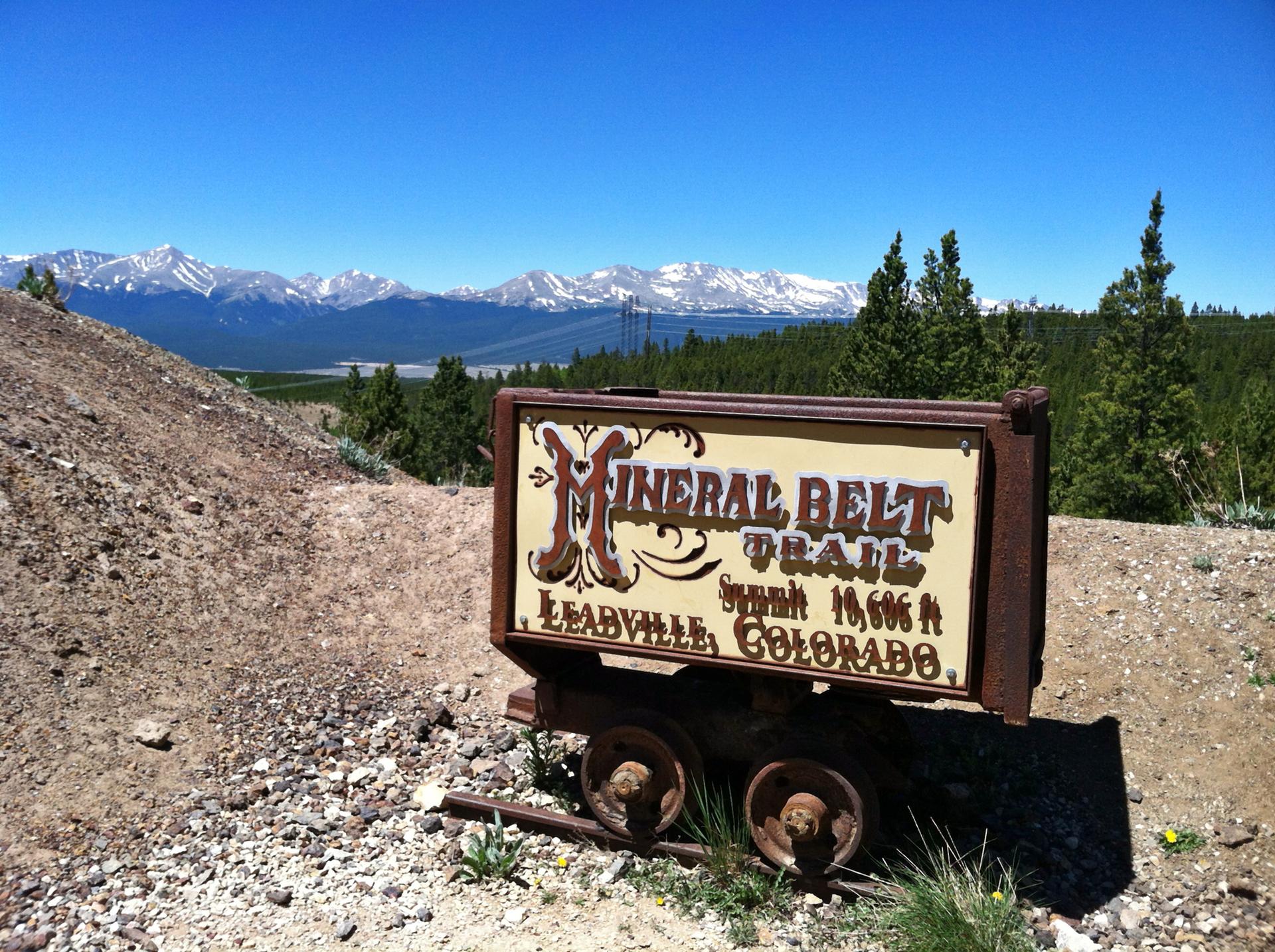 An old mining cart sign overlooks a vast landscape with distant snowy mountains.