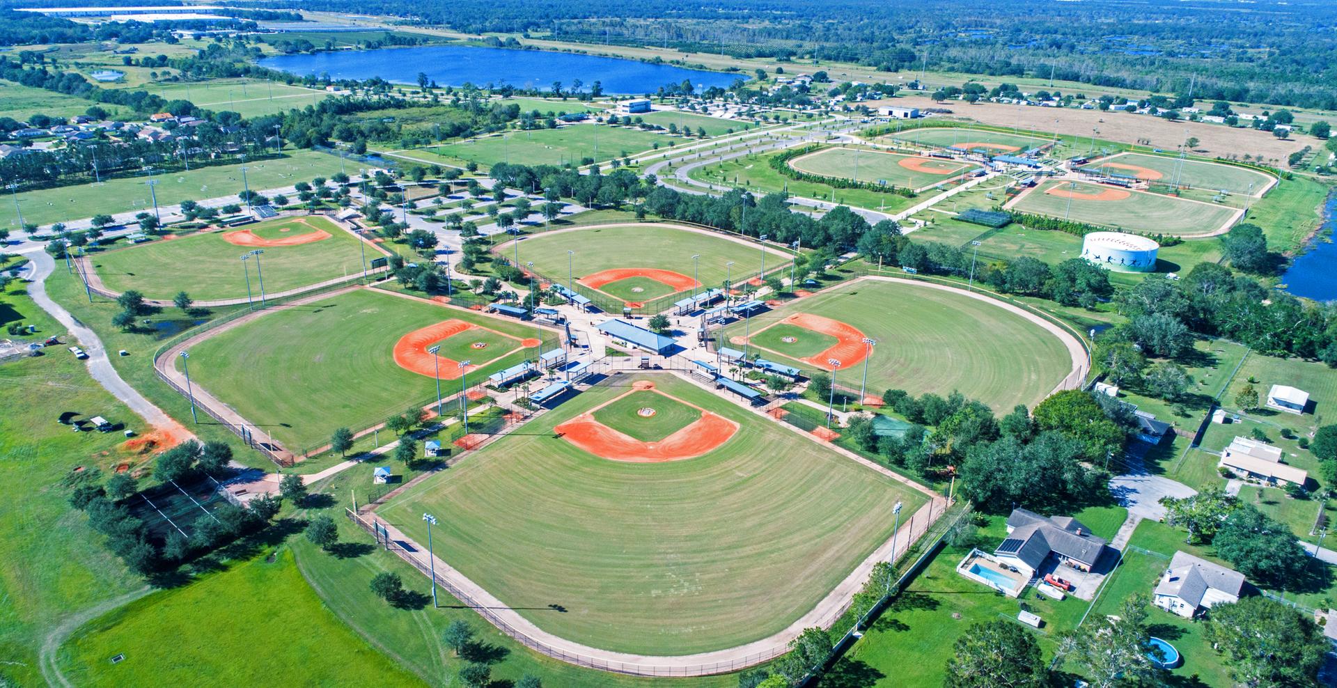 Aerial view of multiple green baseball fields under bright sunlight.