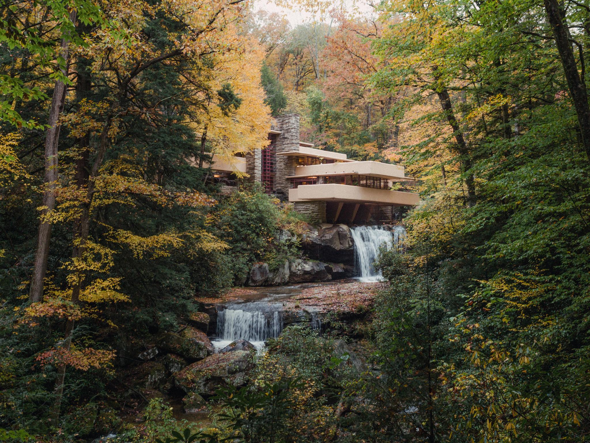 Modern house built over a multi-tiered waterfall in an autumn forest.