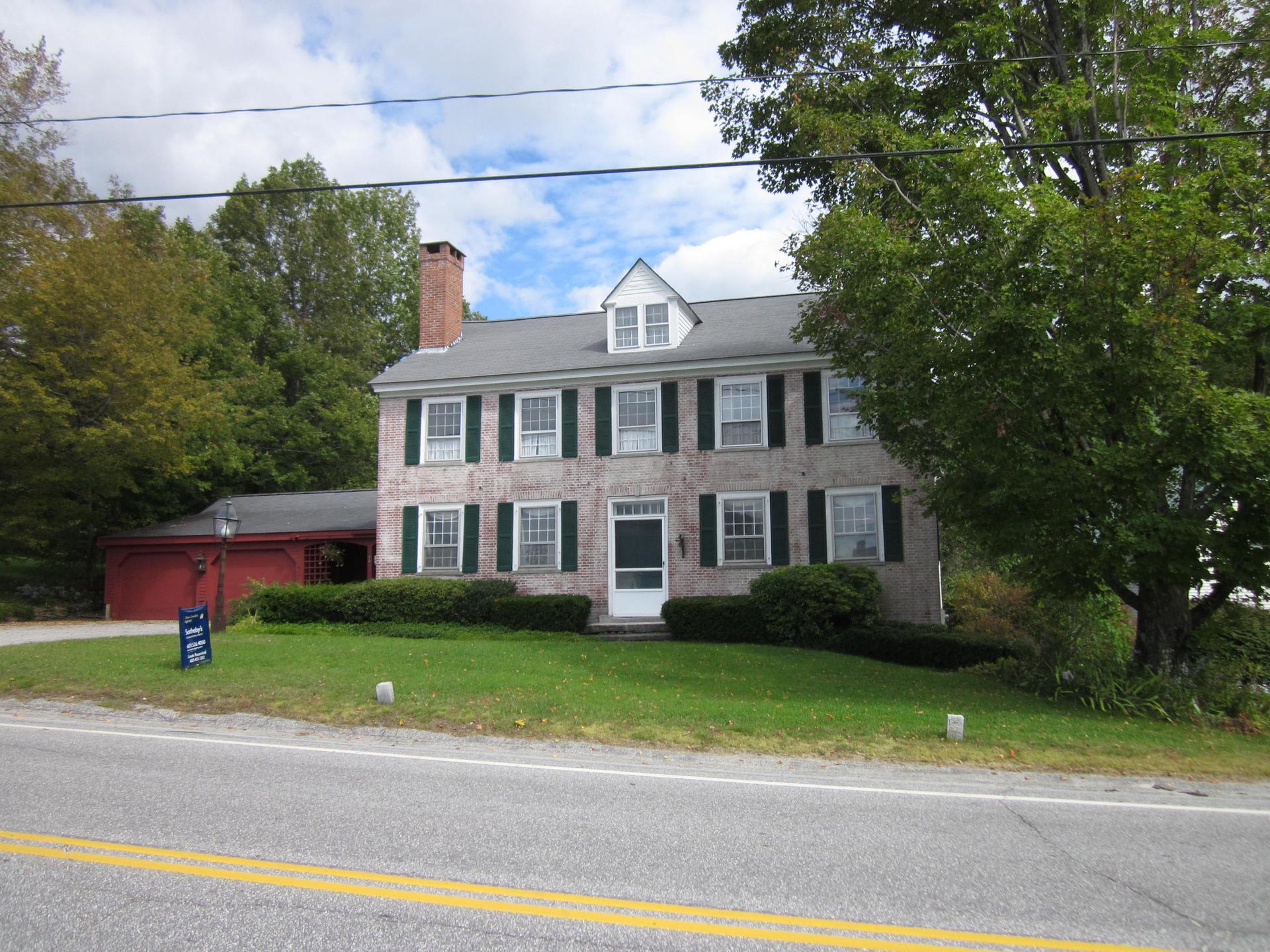 Large two-story house with green shutters and red garage on a sunny day.