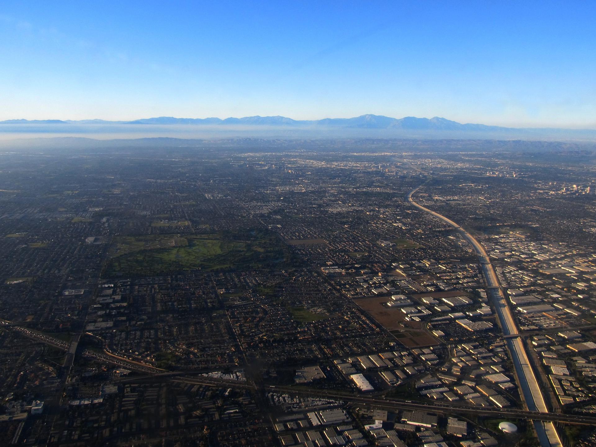 Aerial view of a city with highways, green areas, and distant mountains.