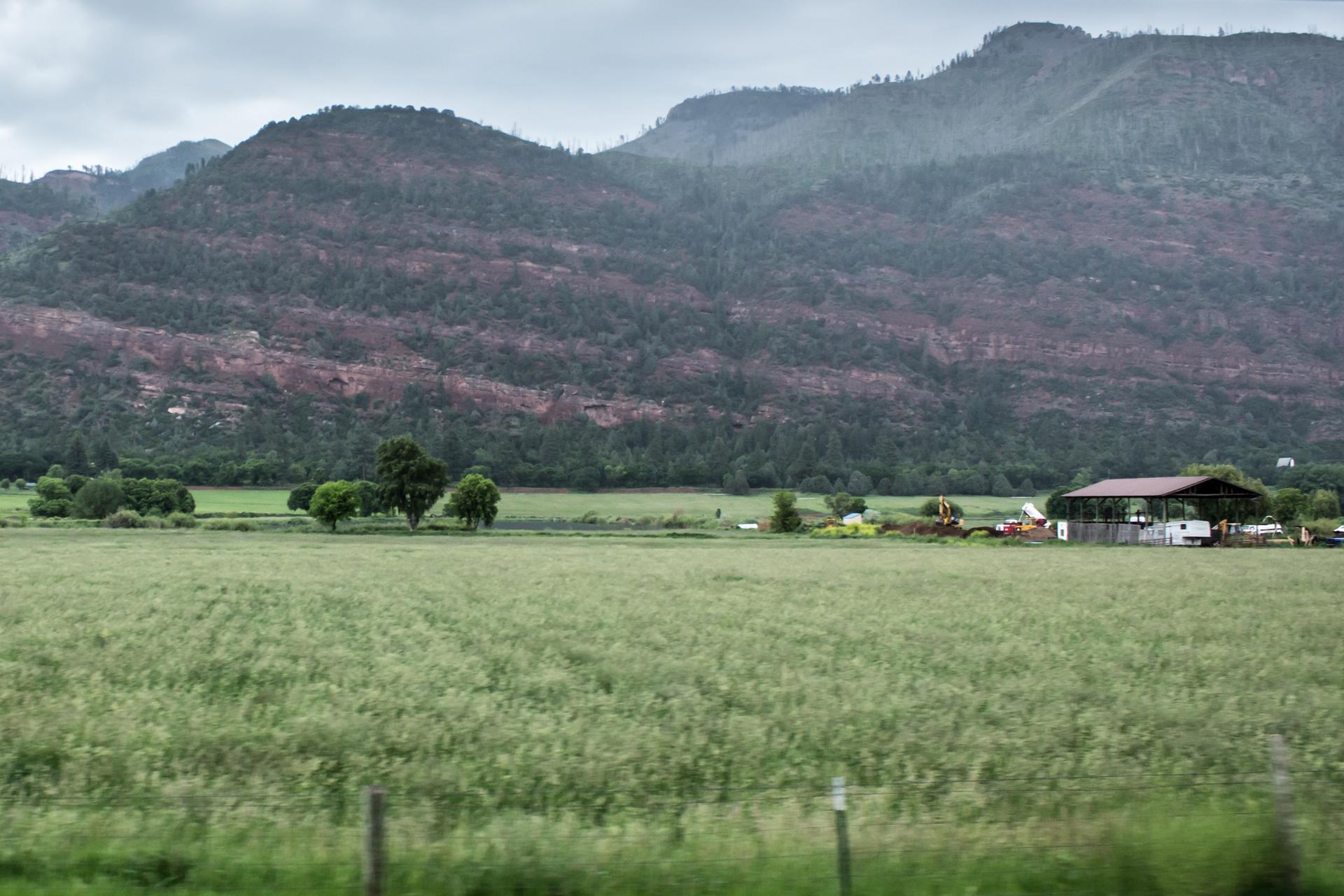 Green field with farm building, dark mountains under an overcast sky.