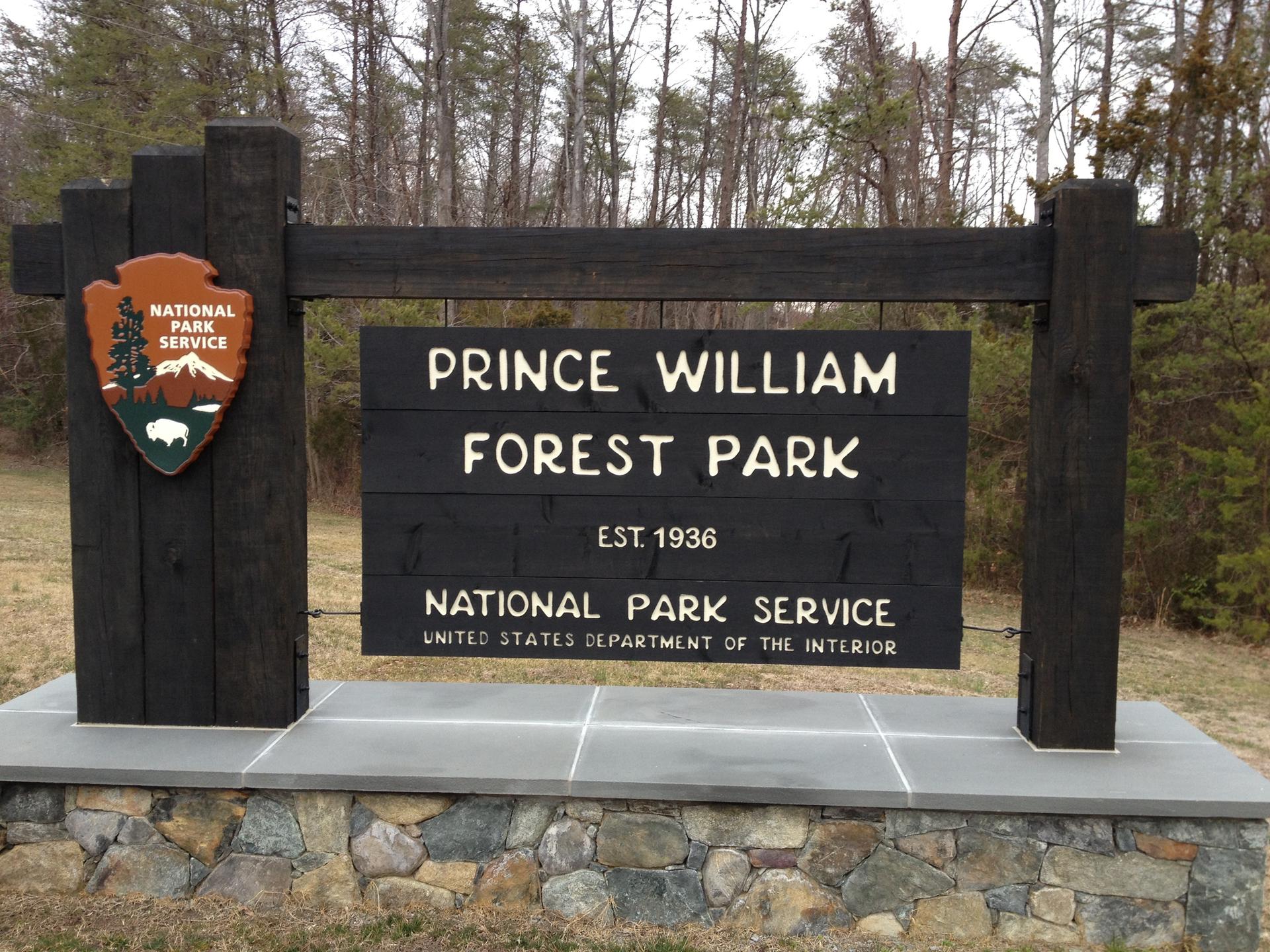 A large wooden sign on a stone base, with bare trees in the background.