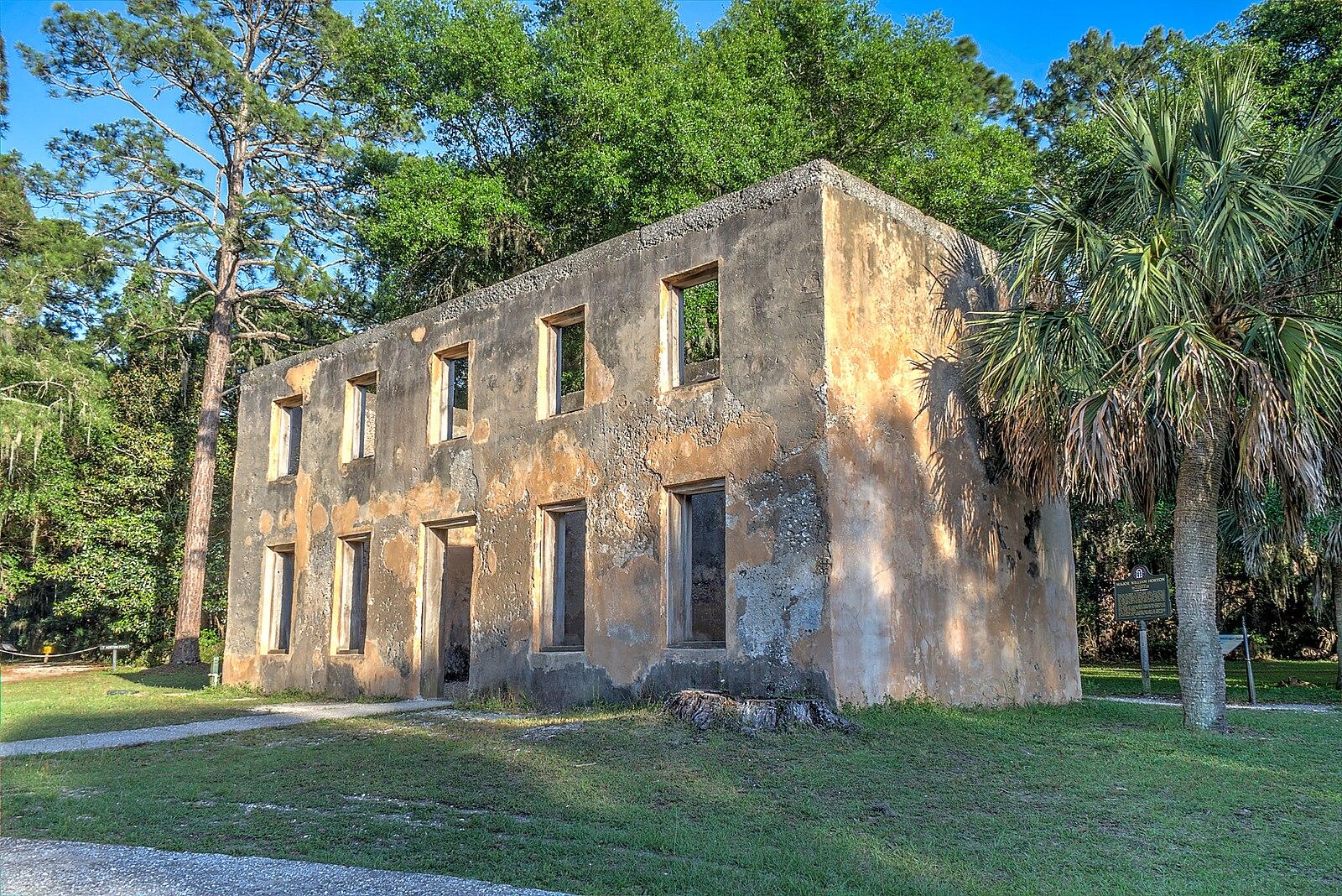 An old stone building with many windows stands on a green lawn near trees.