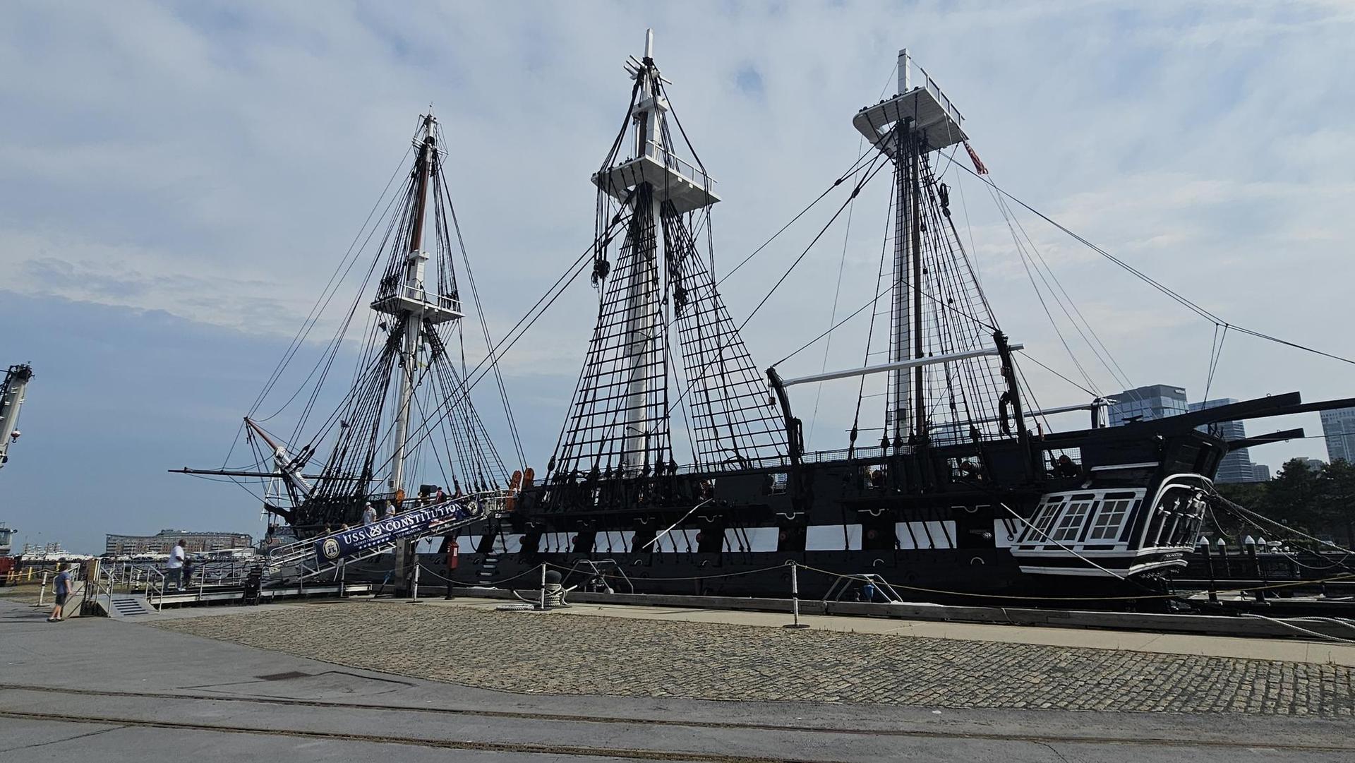 A large, three-masted sailing ship docked on a paved area.