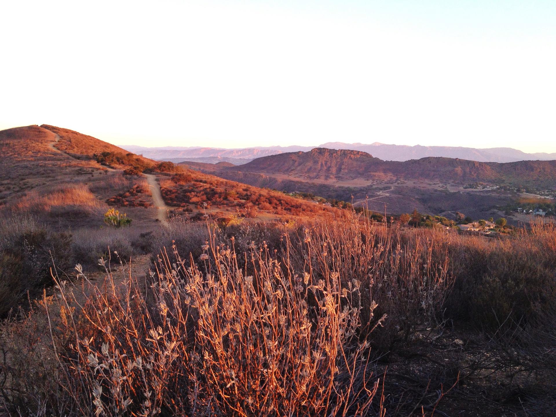 Golden hour light illuminates dry, rolling hills and distant mountains under a vast sky.