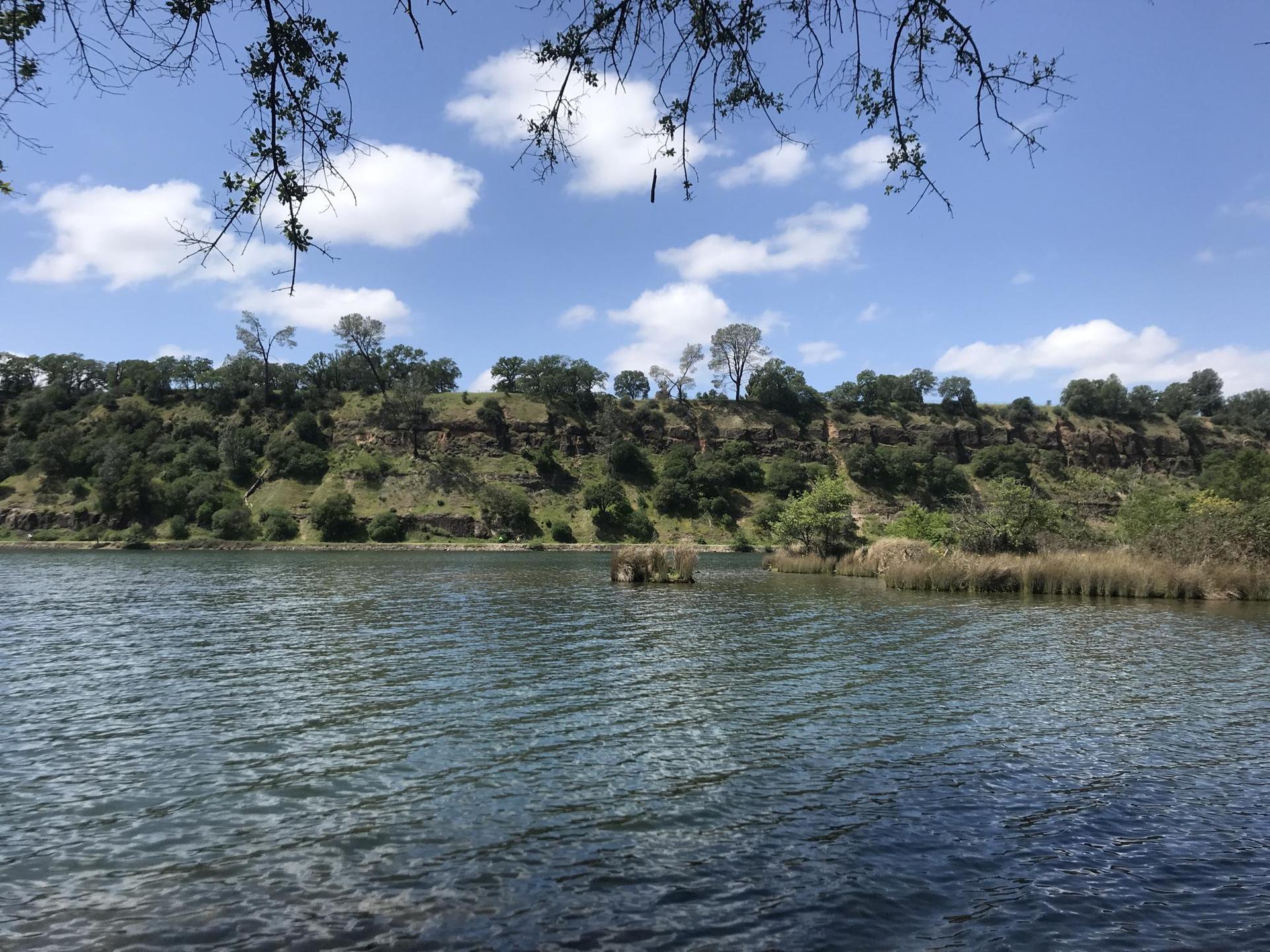 Rippling lake with a green forested hill under a partly cloudy sky.