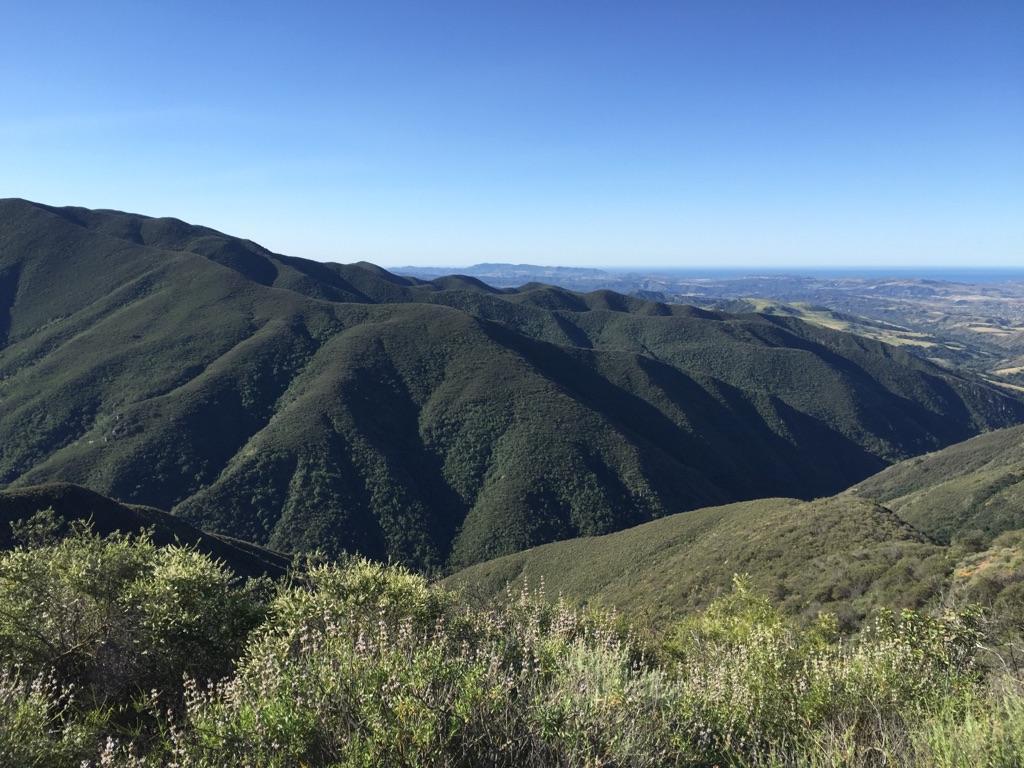 Vast dark green mountains under a clear blue sky, with a distant city.