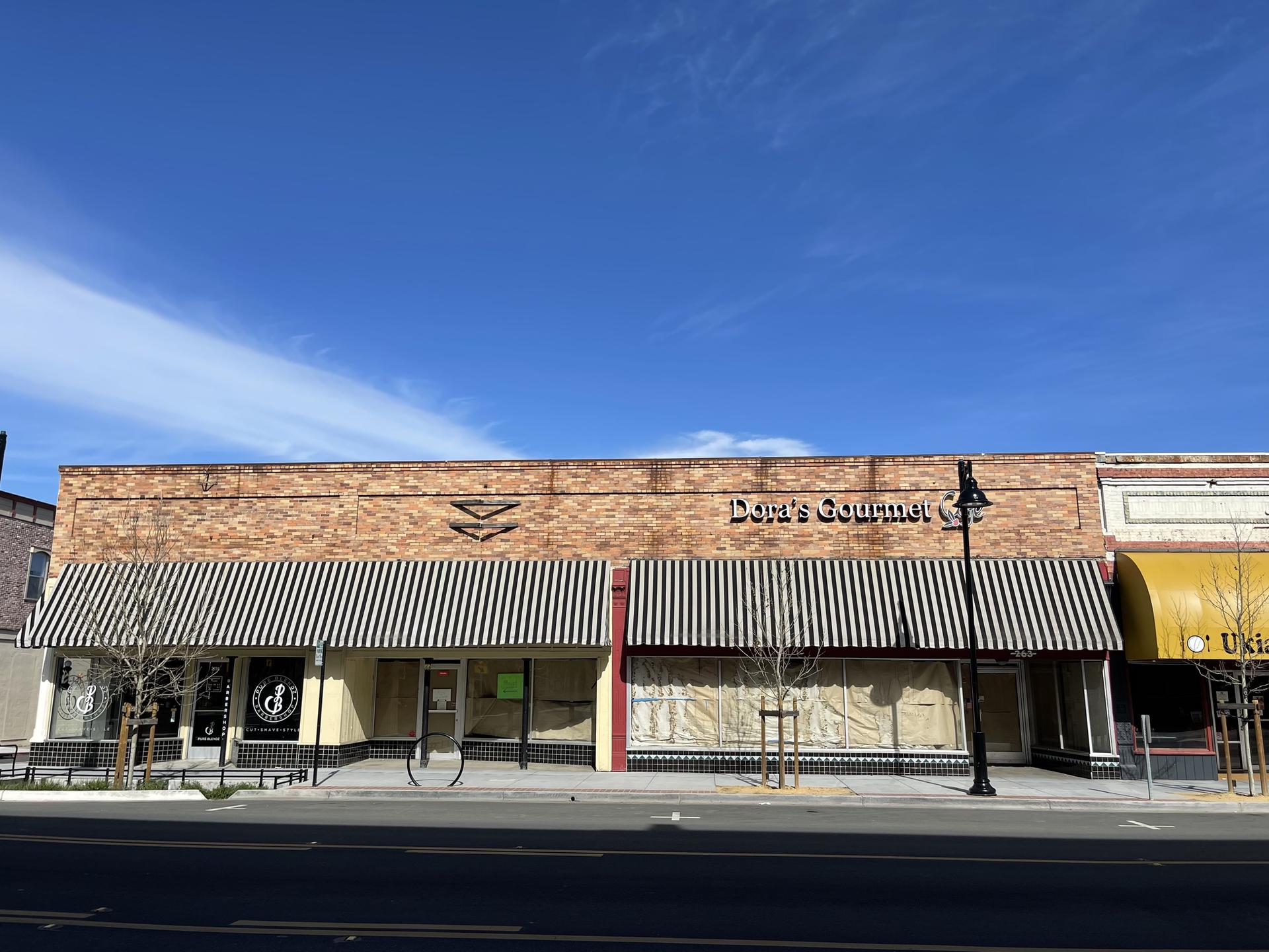 Storefront with striped awnings and a brick facade under a blue sky.