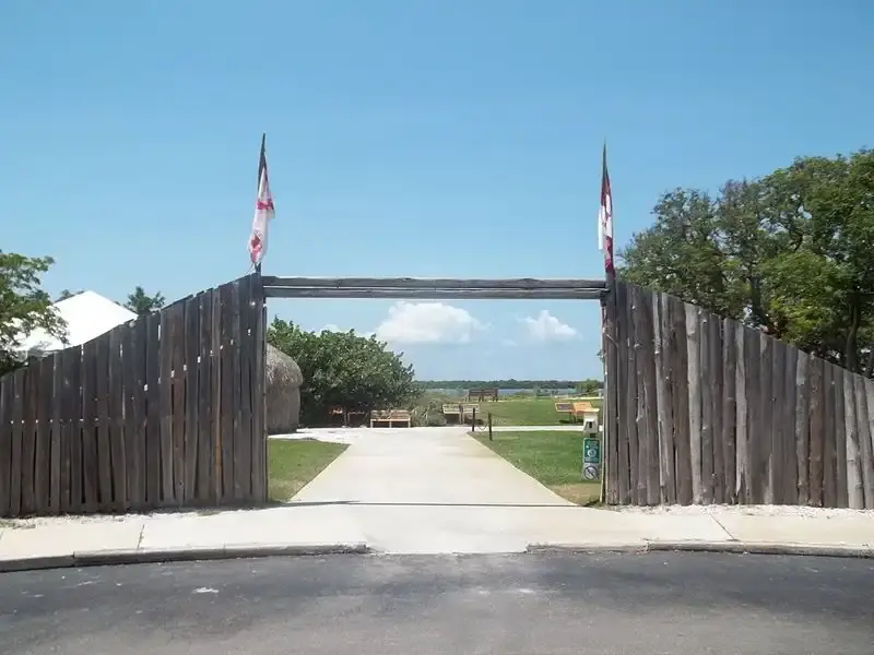 Large wooden gate with flags opens to a sunny grassy field.