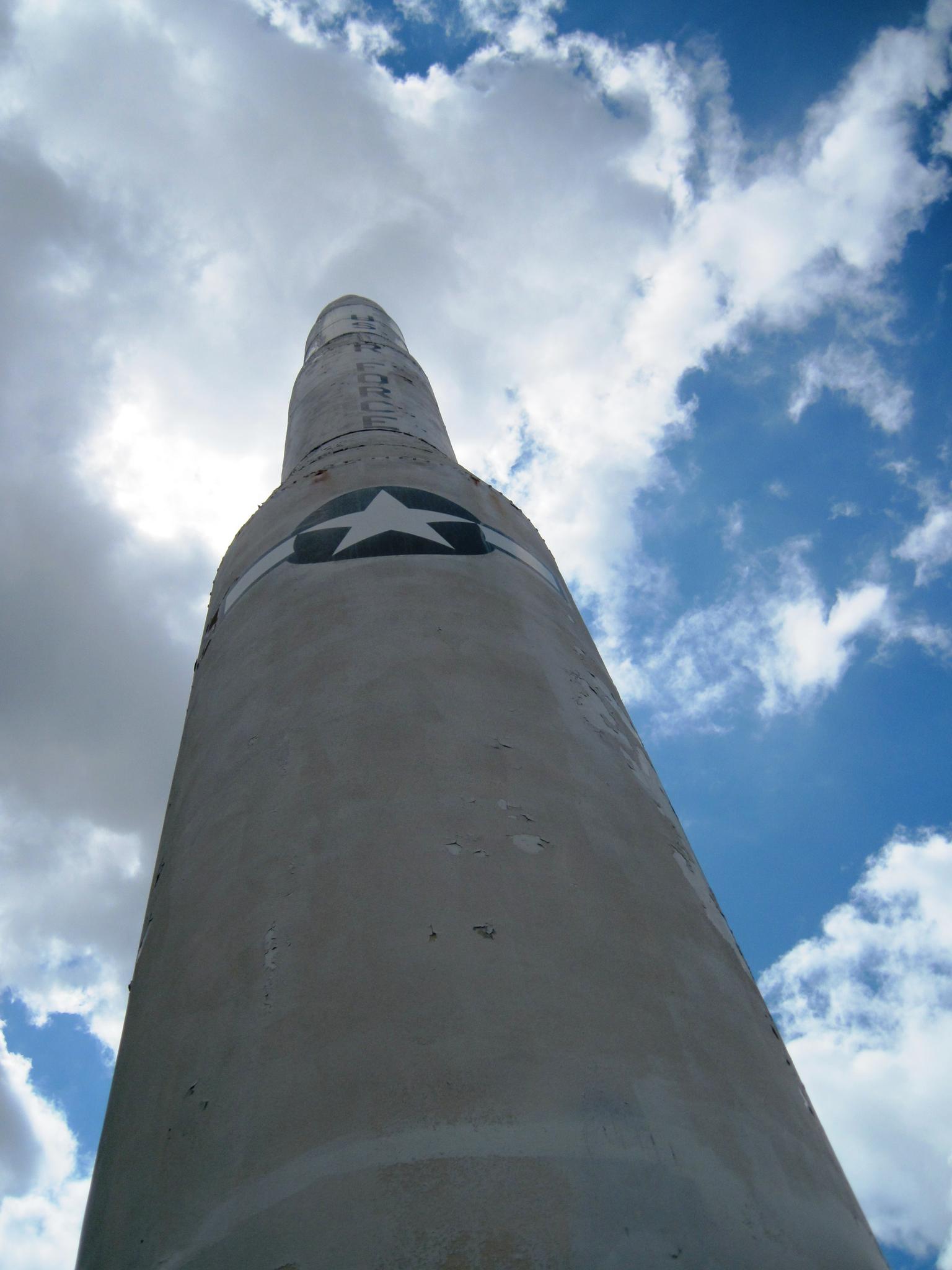 A tall, grey rocket-like structure with a star against a bright, cloudy sky.