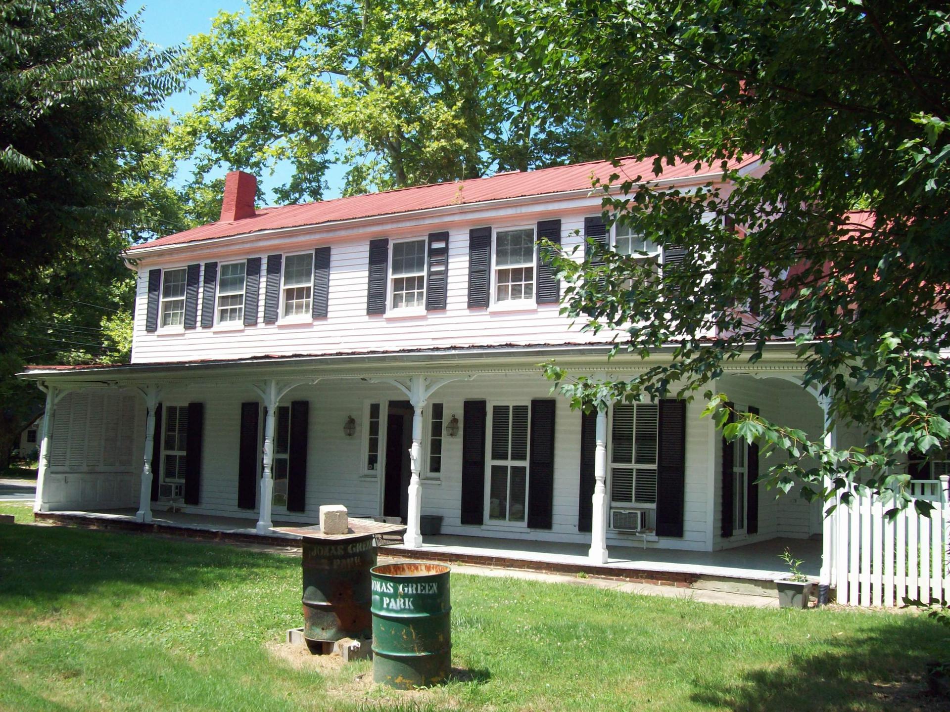White two-story house with red roof and porch on a bright, sunny day.