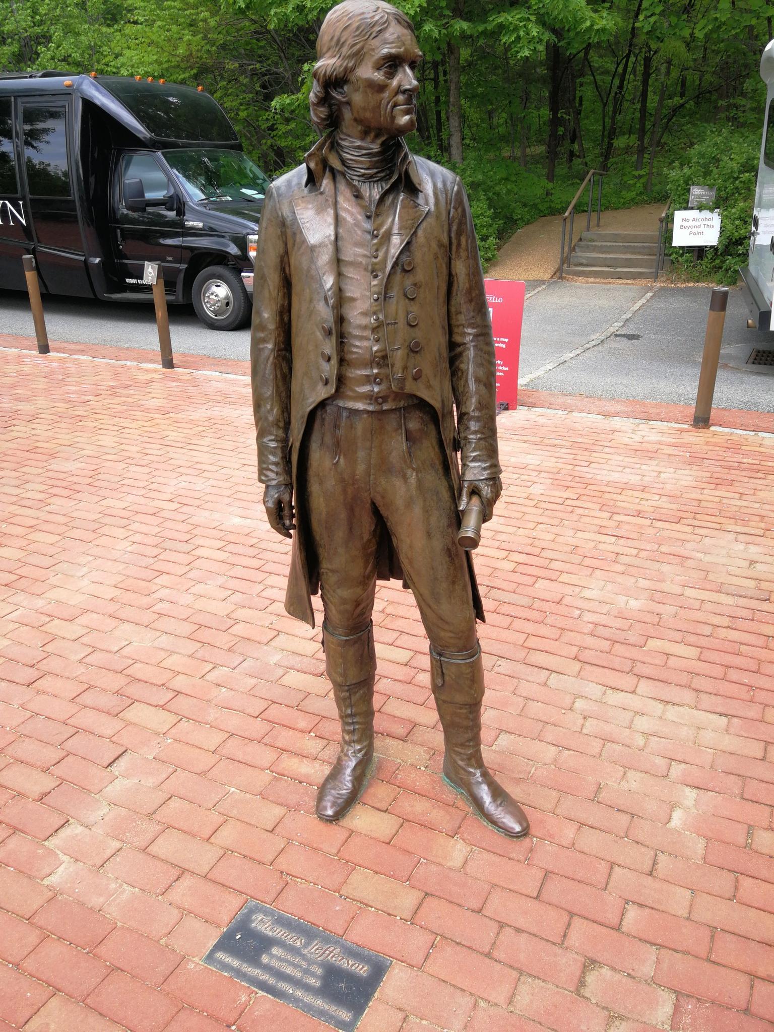 Bronze statue of a man in historical clothing on a brick path.