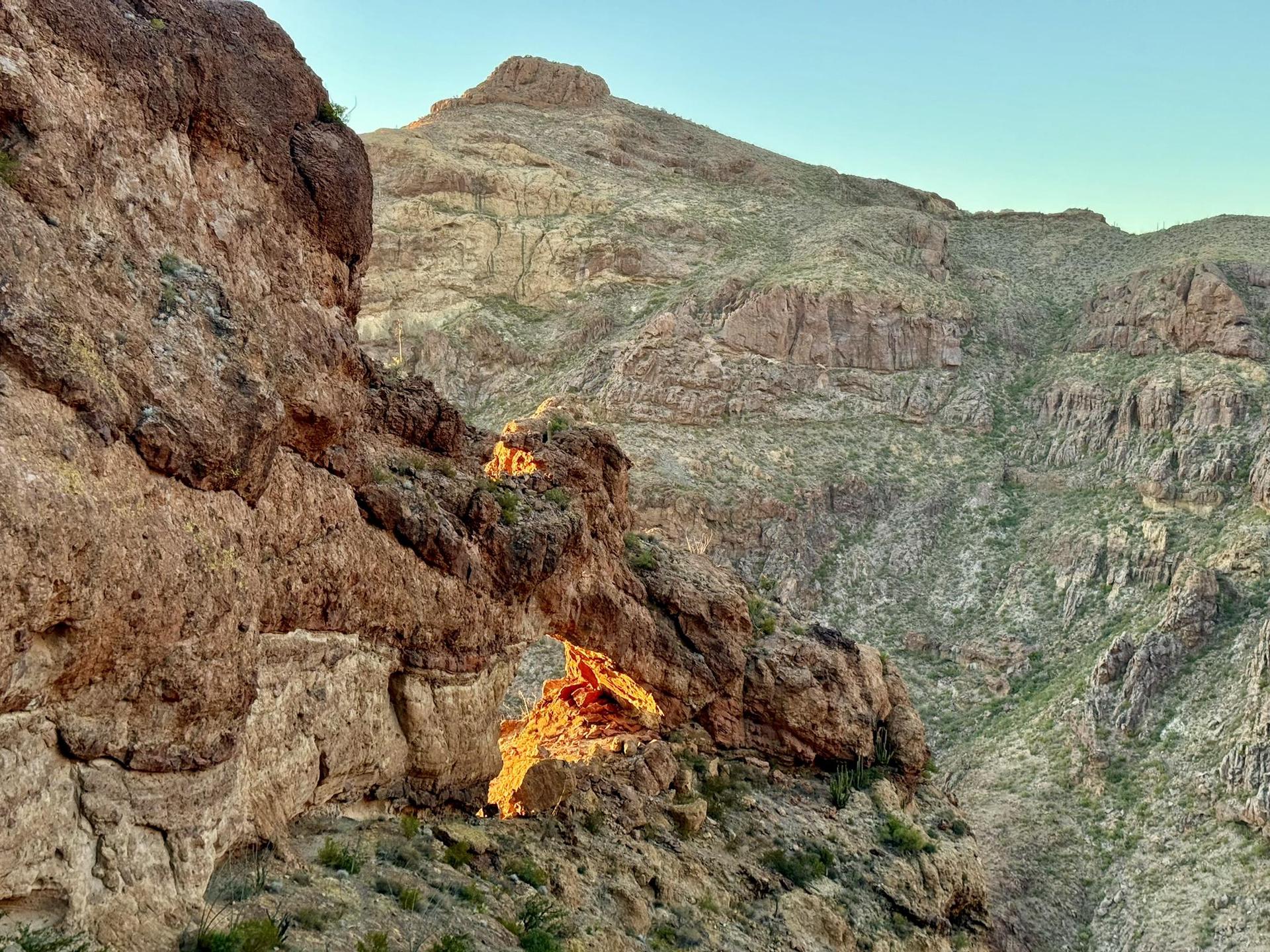 Golden light illuminates a natural rock arch in a rugged desert canyon.