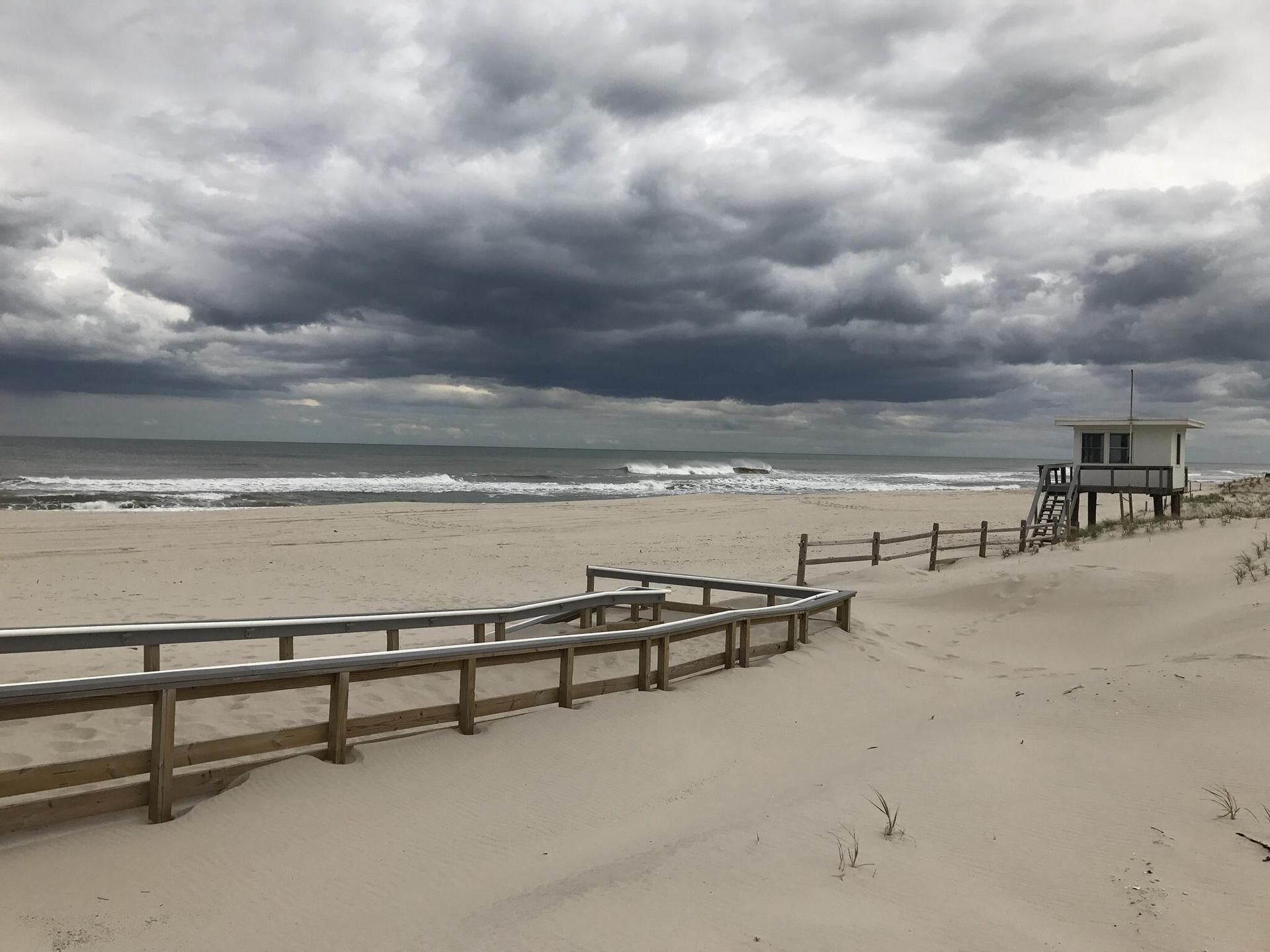 Empty beach with a lifeguard stand, boardwalk, and dark, cloudy sky.