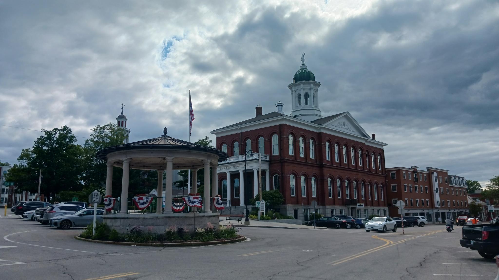 A town square with a gazebo, brick building, and overcast sky.