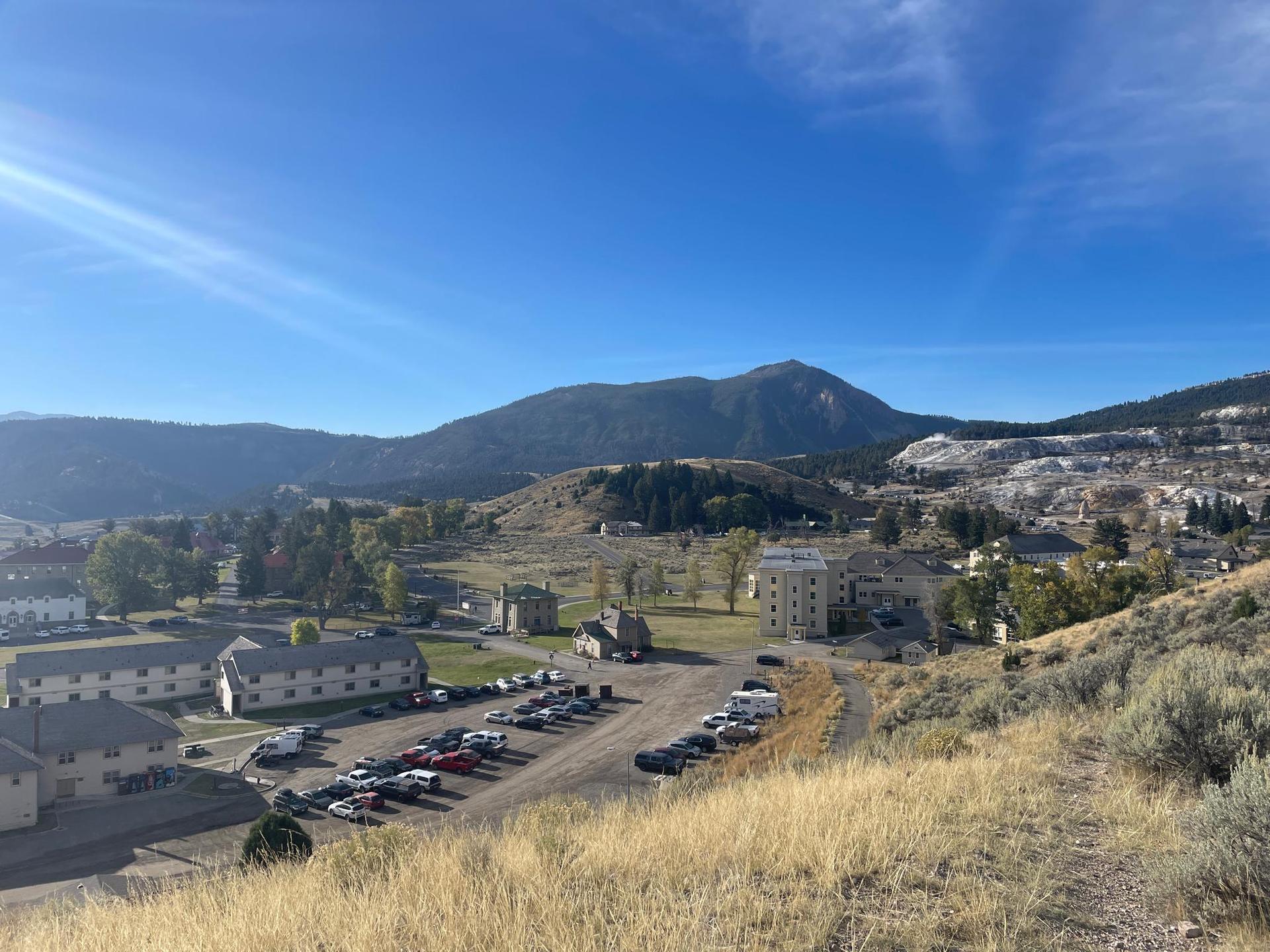 Sunny overlook of a town with buildings and mountains under a clear blue sky.