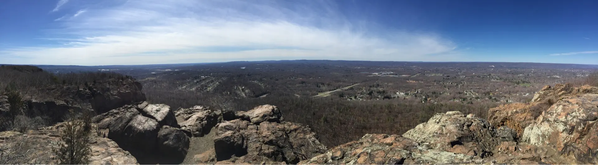 Panoramic view from rocky cliffs overlooking a vast landscape under a clear sky.